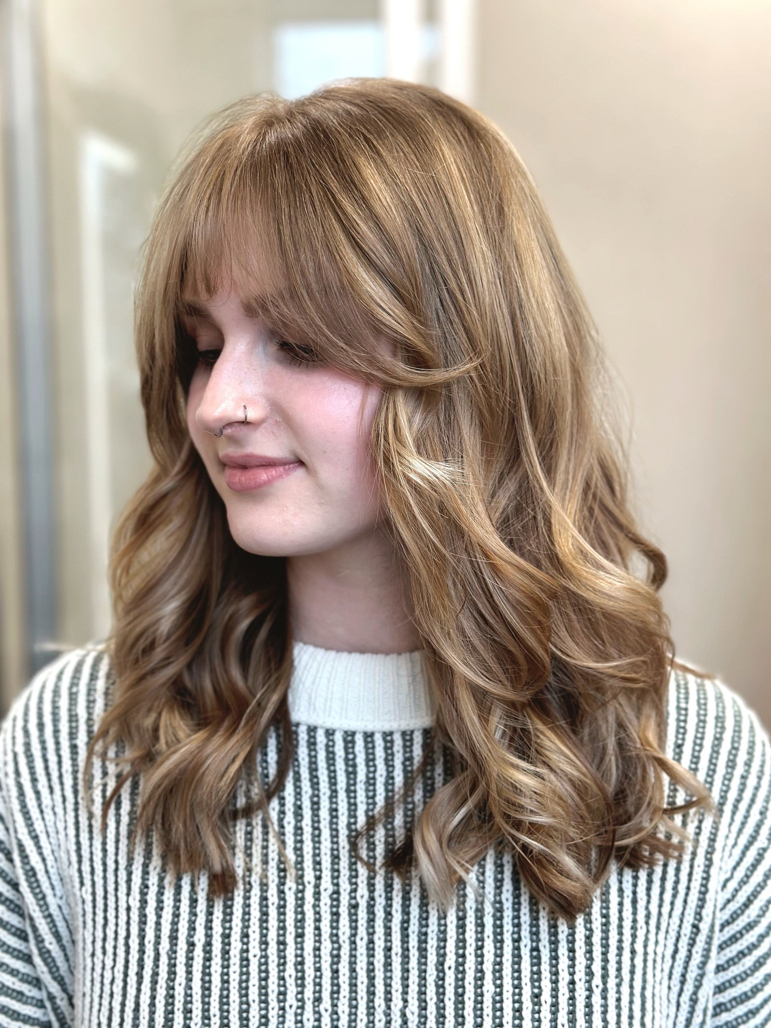 Photo of a client with long hair, soft waves, long curtain bangs, and lots of highlights and low lights.