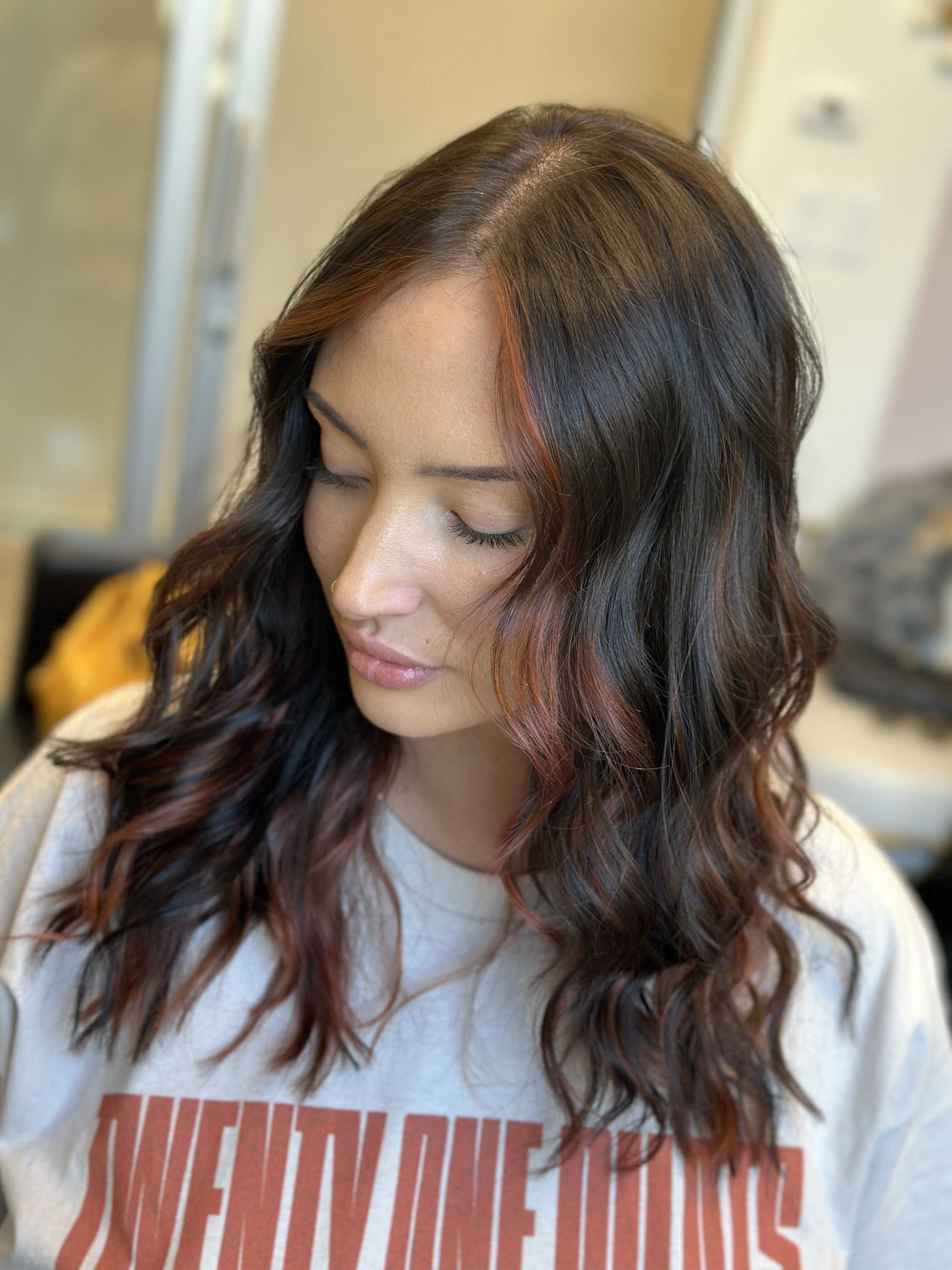 Photo of a client with long, dark hair and face framing red highlights. 