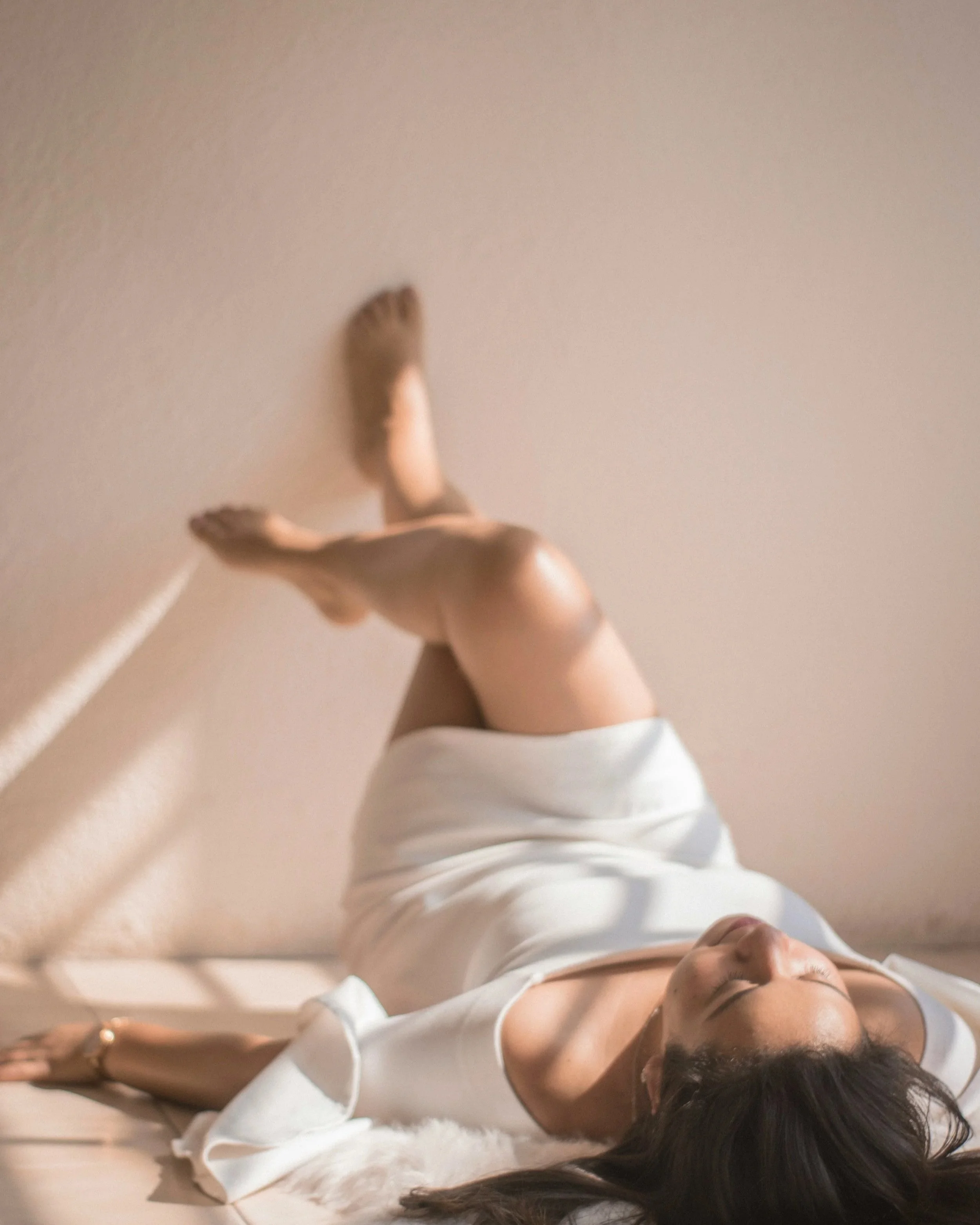 Woman lying back on white fabric with legs raised, depicting somatic release and body awareness