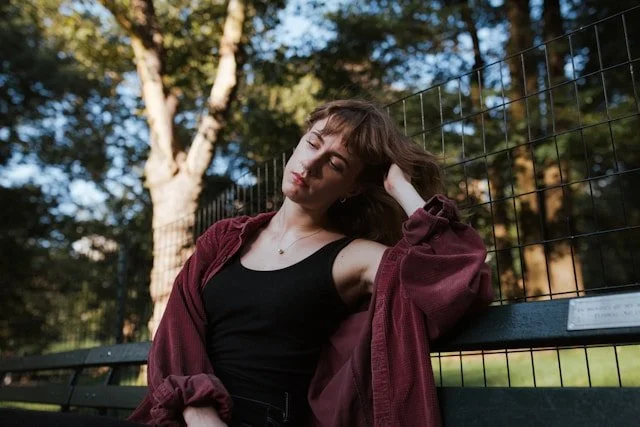 Woman sitting on a bench outdoors among trees, feeling disconnected from herself