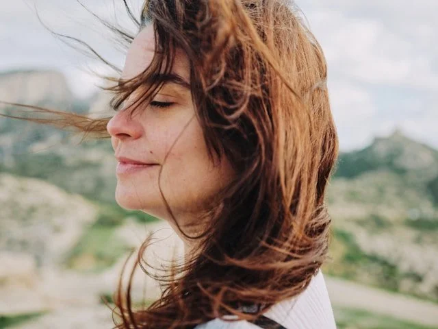 Woman with eyes closed, wind in her hair, embodying self-loyalty and inner freedom