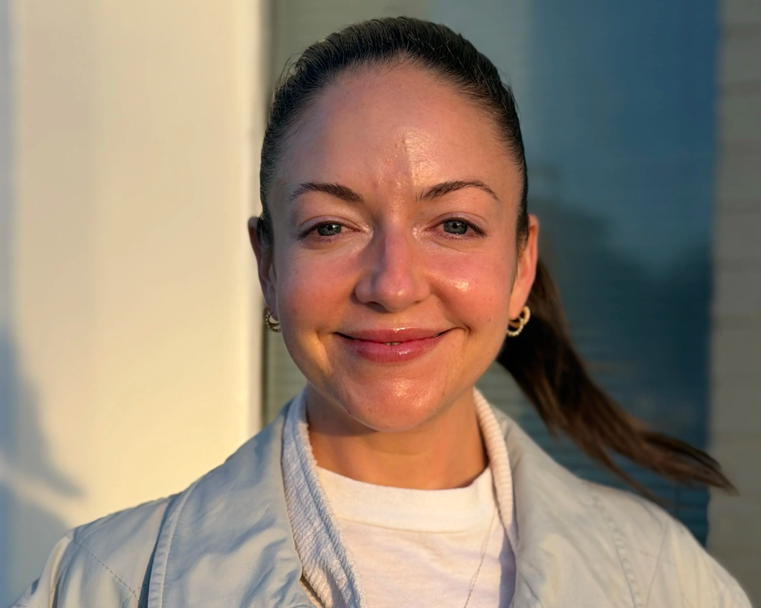 Woman smiling naturally with bare face in warm light, showing authenticity over managed appearance
