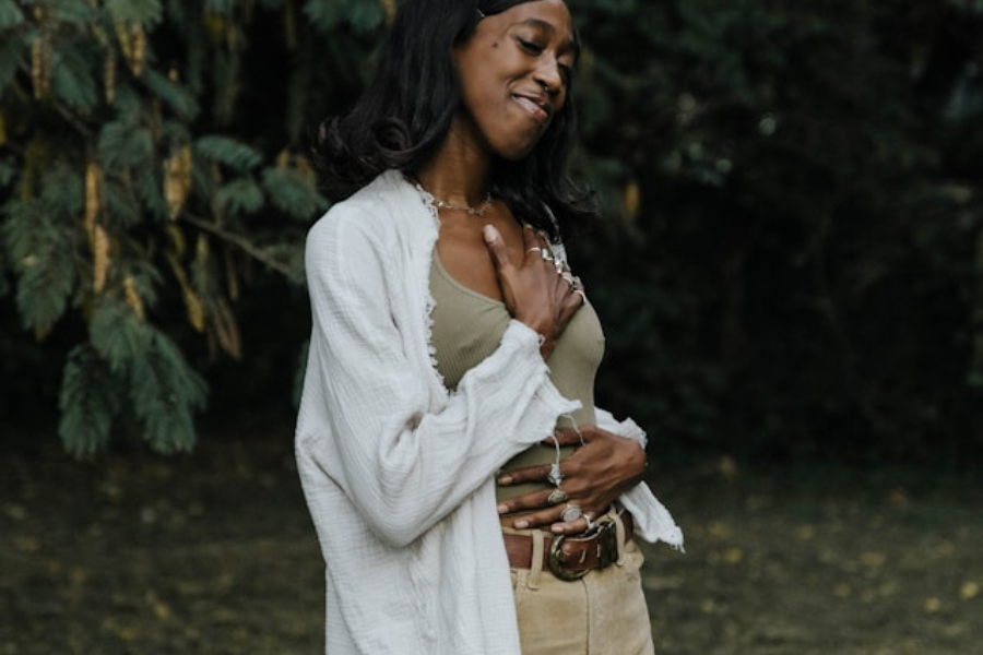 Woman in white shirt holding herself with hand over heart in forest