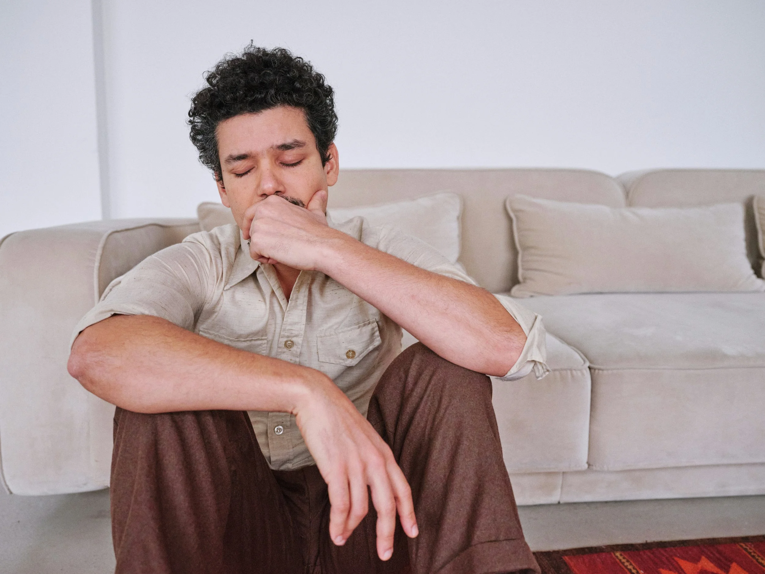 Man sitting on couch with hand to face looking withdrawn and in contemplation