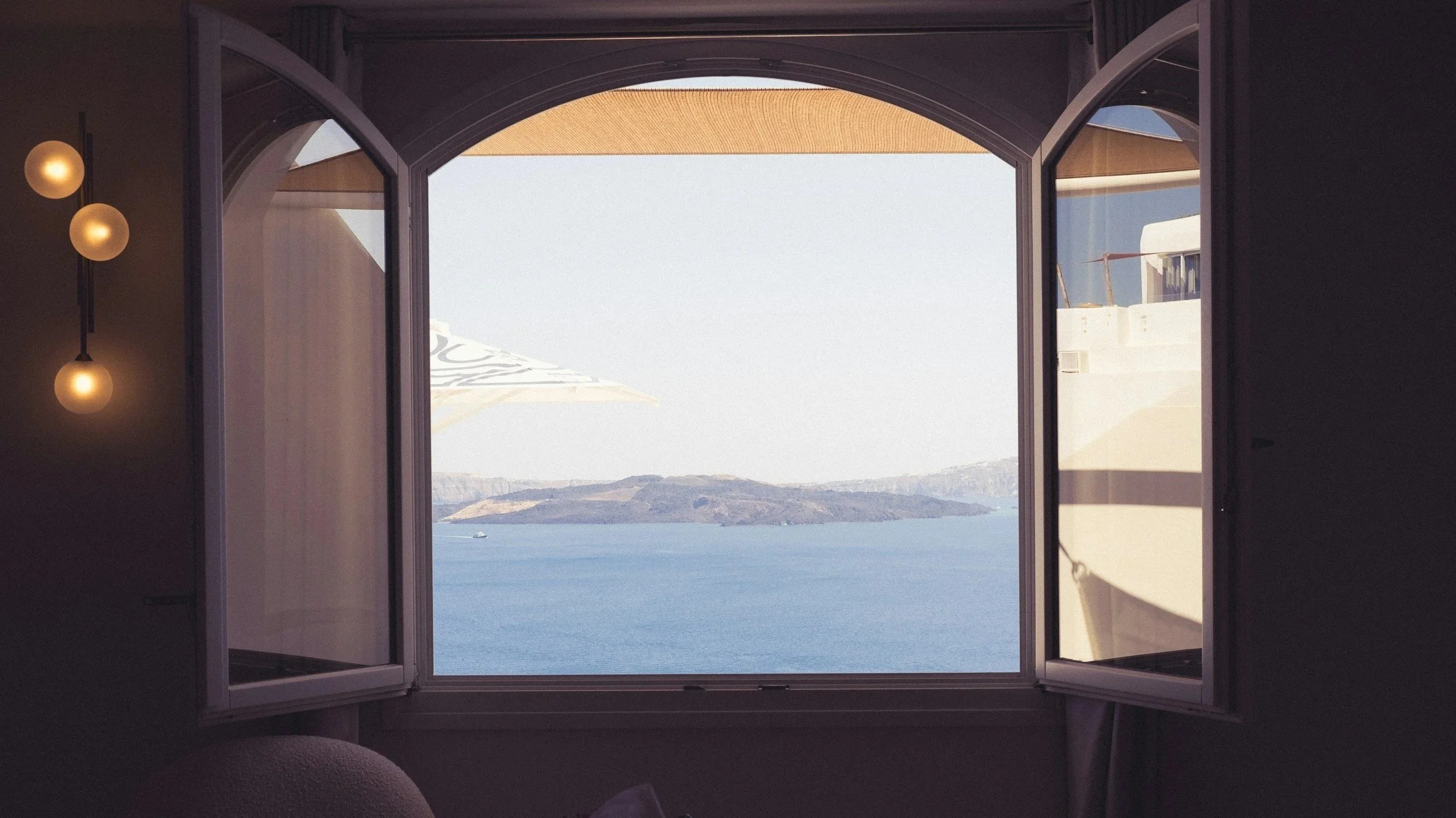 View of the ocean and distant land through an open window with curtains inside a room, representing openness.
