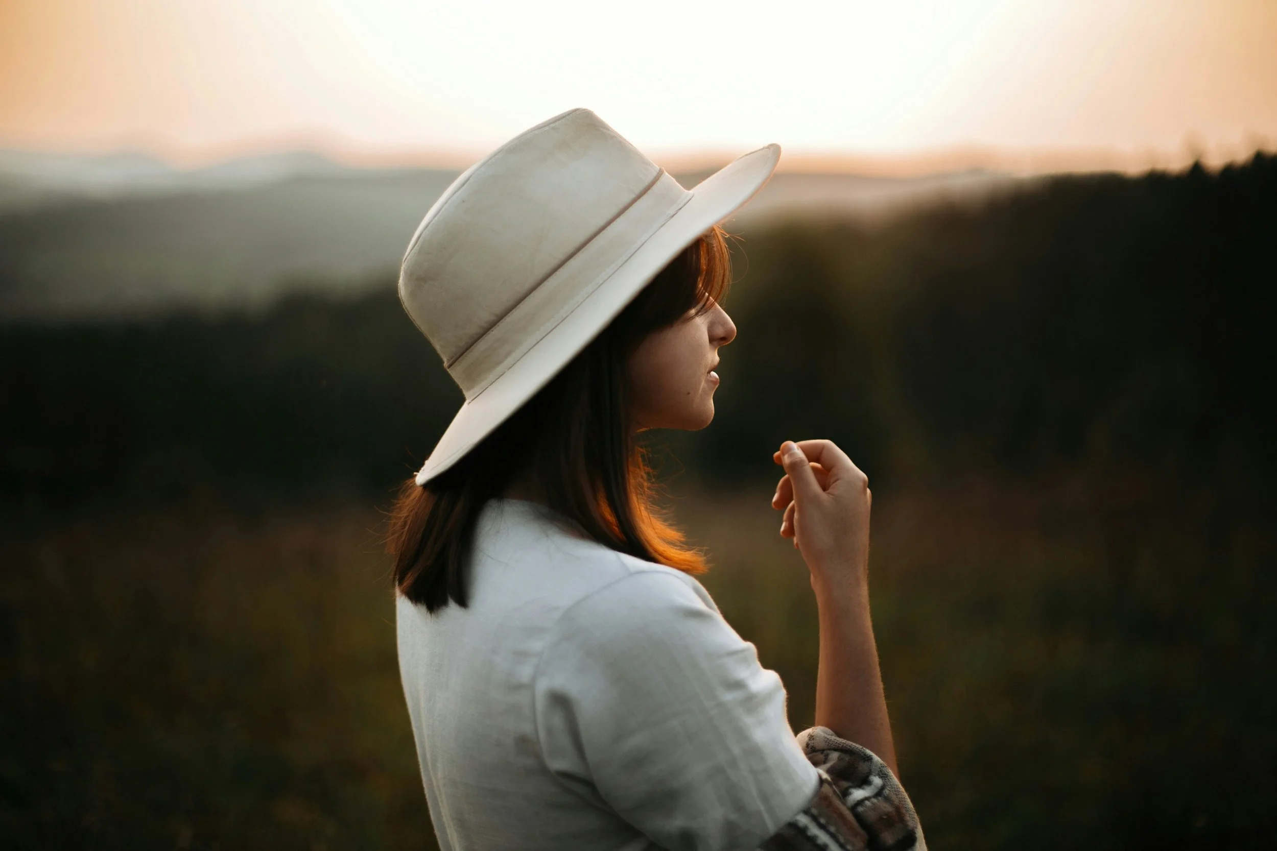 Woman in a hat sitting quietly outdoors at sunset, reflecting on self-trust and self-loyalty