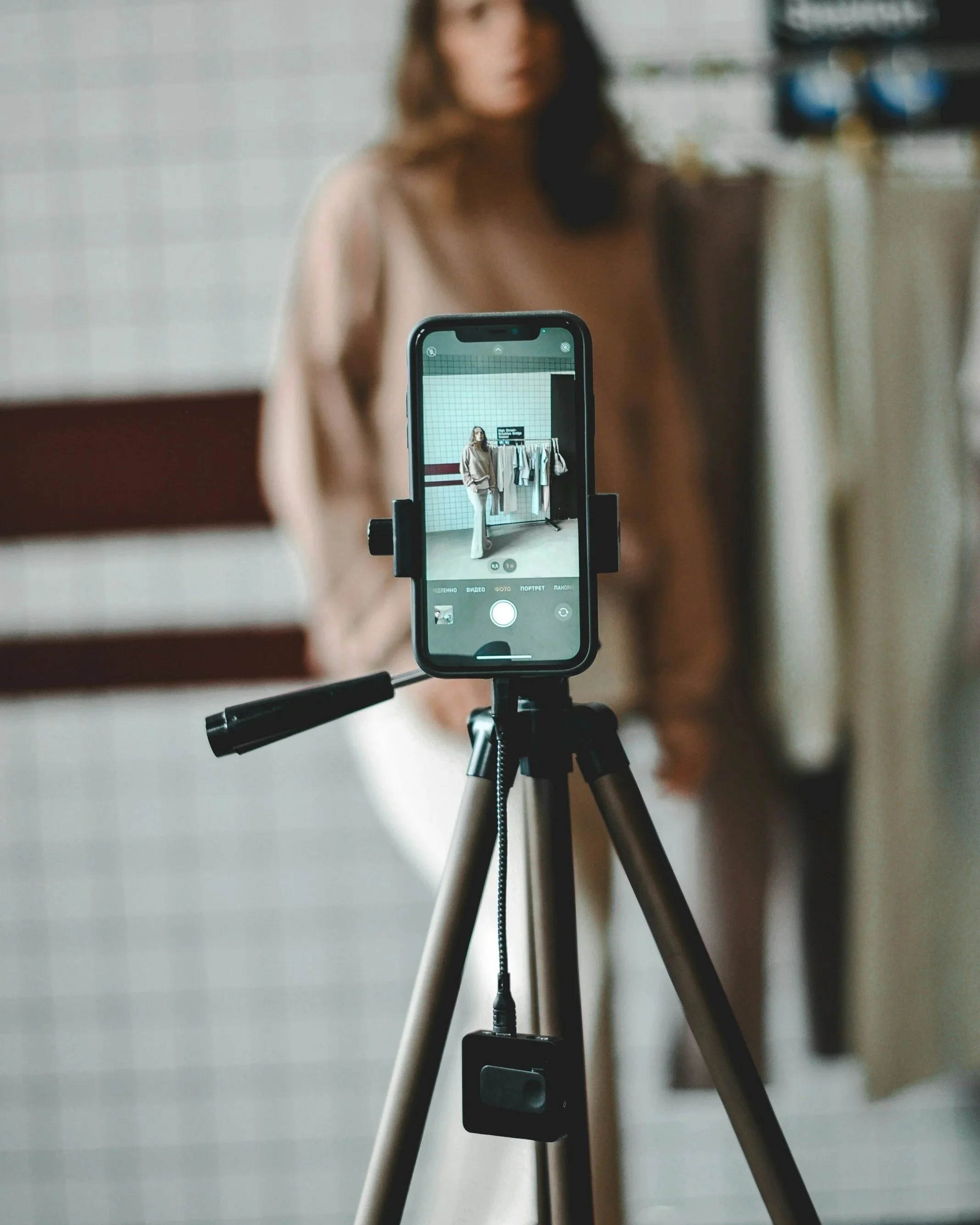 Woman standing behind a tripod filming social media content, representing the performance demand that the body resists