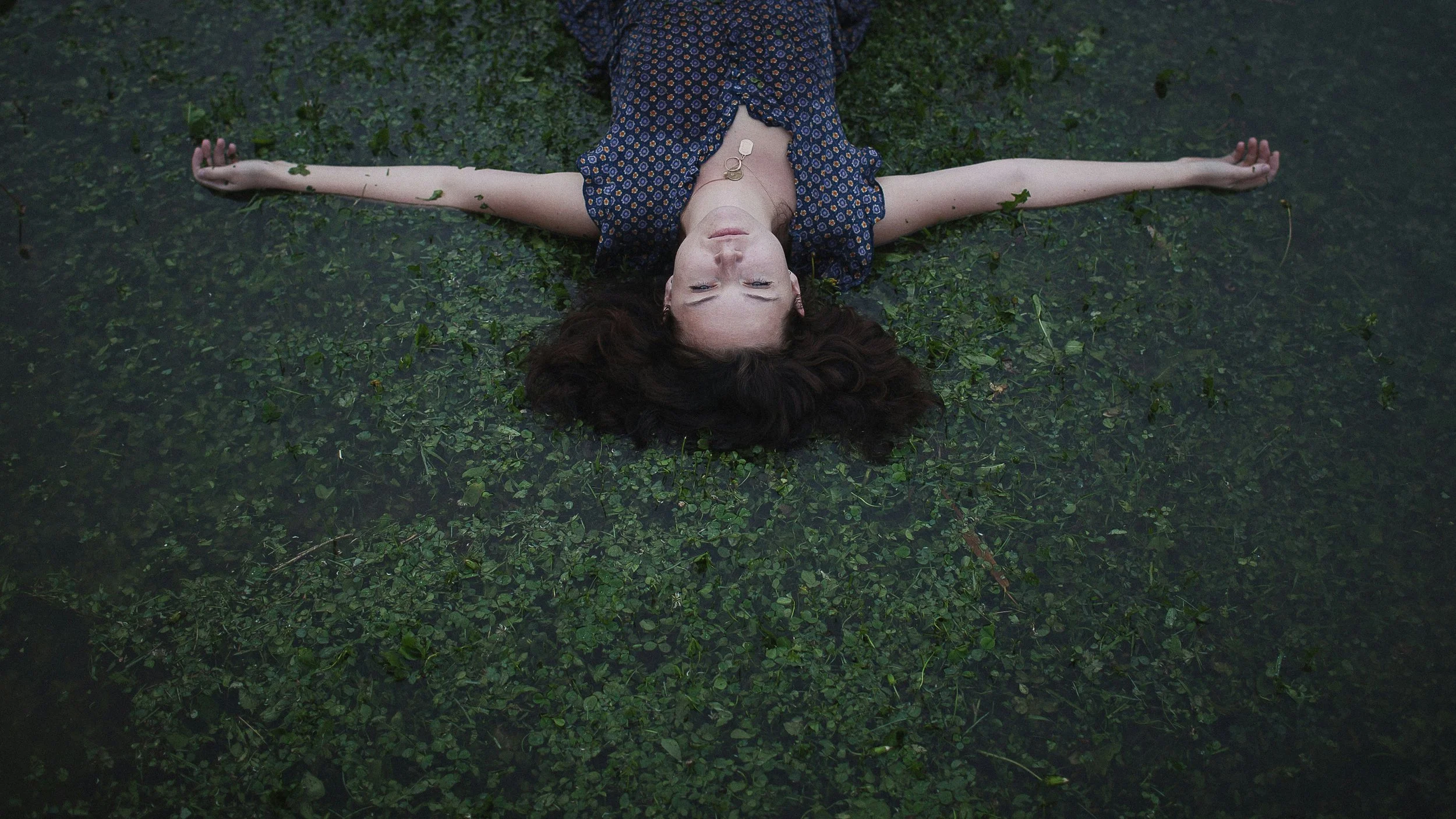 Woman lying in a field of clover with arms open and eyes closed, embodying somatic release and the process of letting go of self-abandonment patterns held in the body.