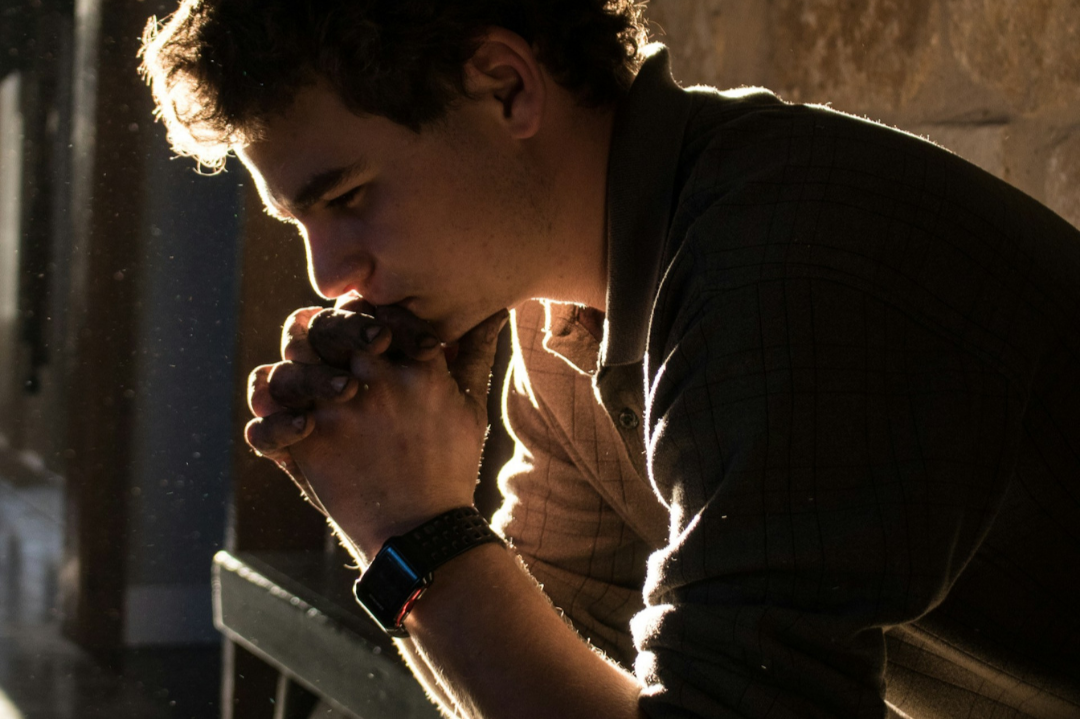 Person with hands clasped in prayer or contemplation with golden light