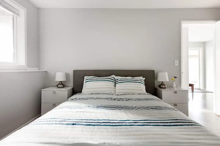 A bedroom with a bed, two nightstands with lamps, and a window to the left.