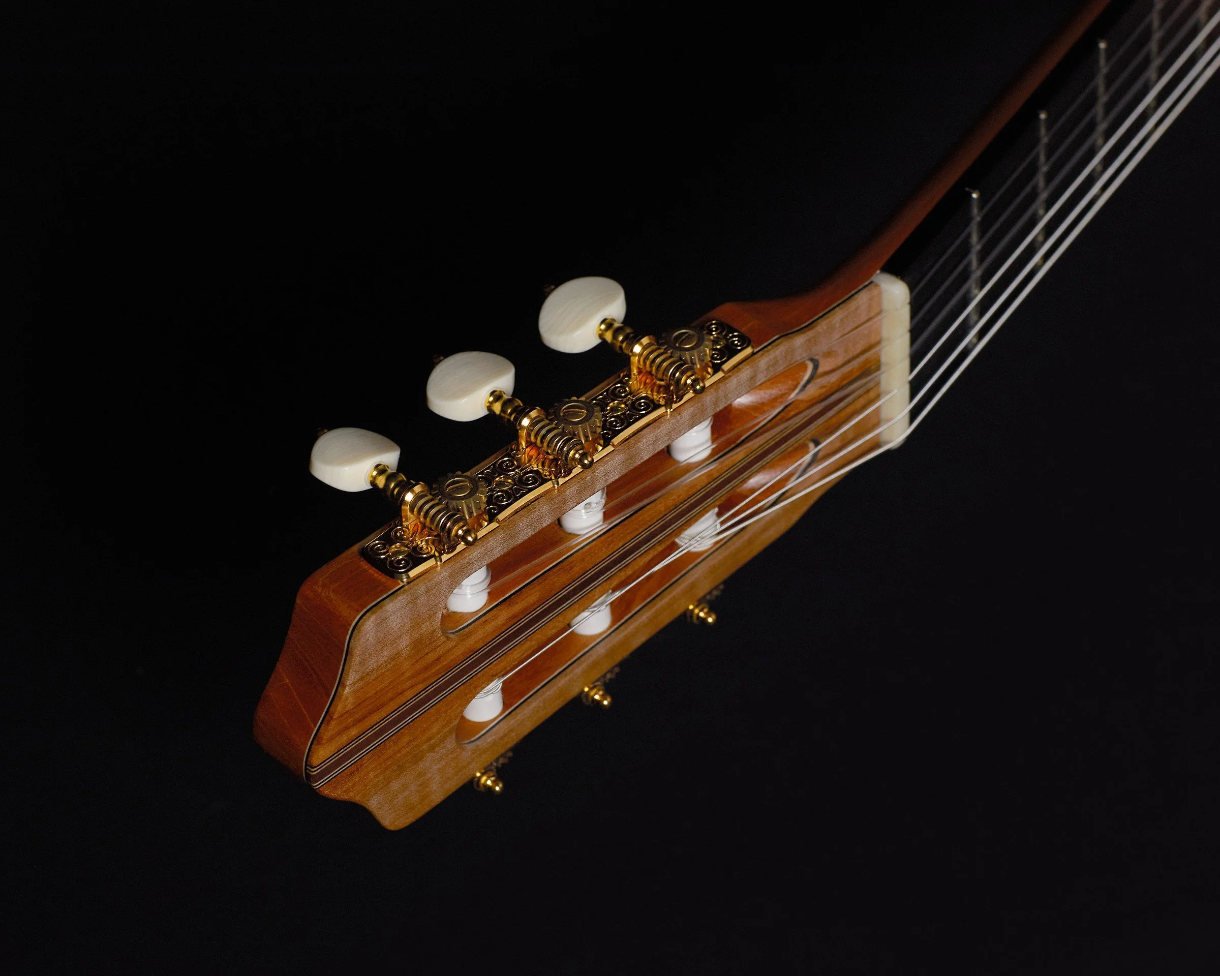 Slotted headstock and gold tuning machines on a handmade DeMers classical guitar, photographed against a black background.