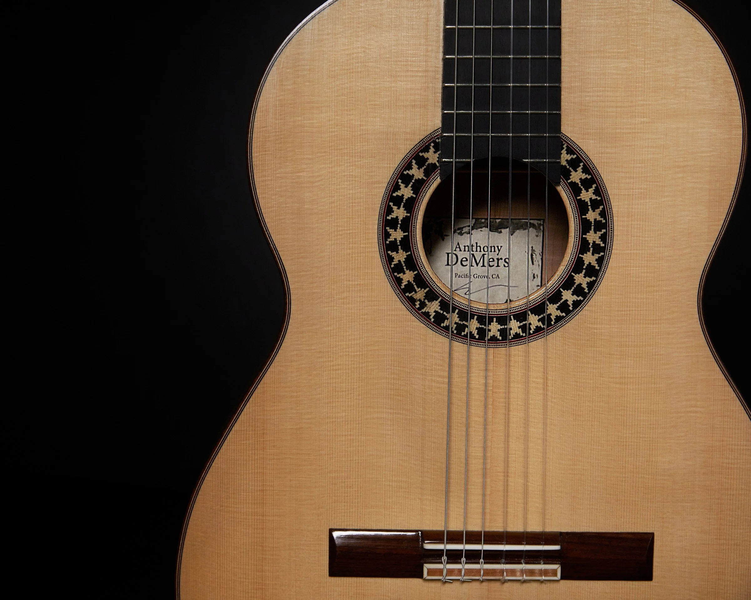 Front detail of a handmade DeMers classical guitar showing the rosette, maker’s label, bridge, strings, and soundboard.