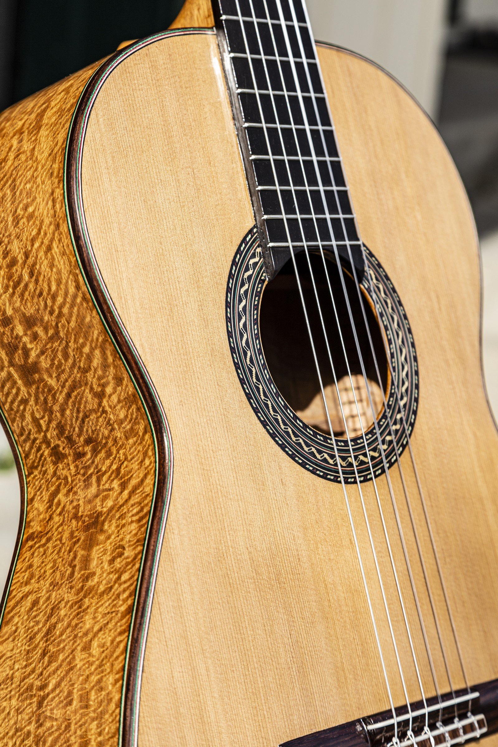 Close view of a handmade DeMers classical guitar showing the rosette, soundboard, figured side wood, binding, and decorative purfling.