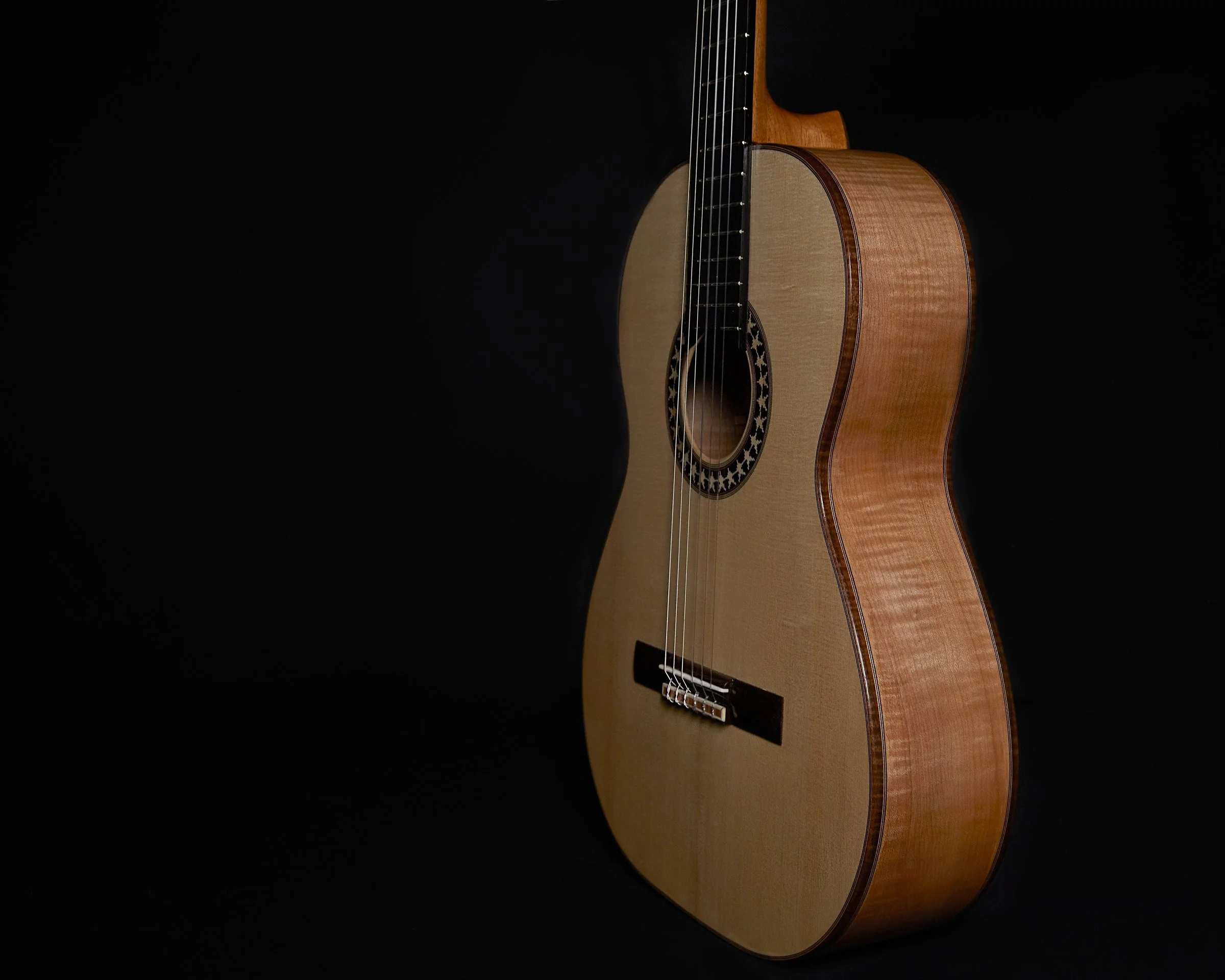 Three-quarter studio view of a handmade DeMers classical guitar showing the soundboard, rosette, bridge, and figured sides.