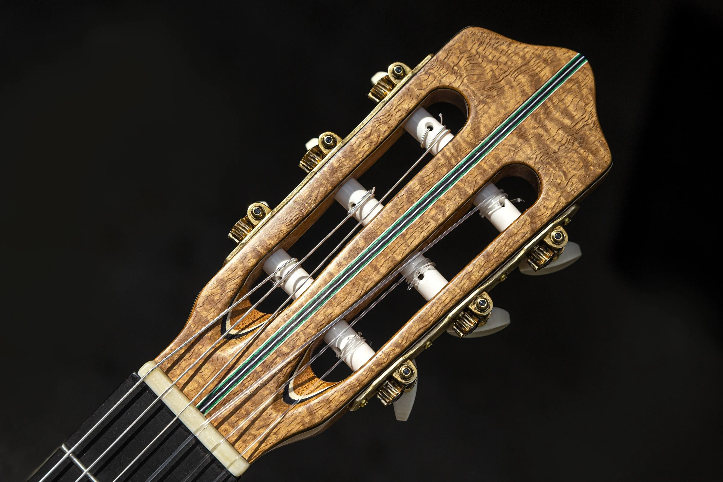 Figured-wood slotted headstock with a decorative center strip and gold tuning machines on a handmade DeMers classical guitar.