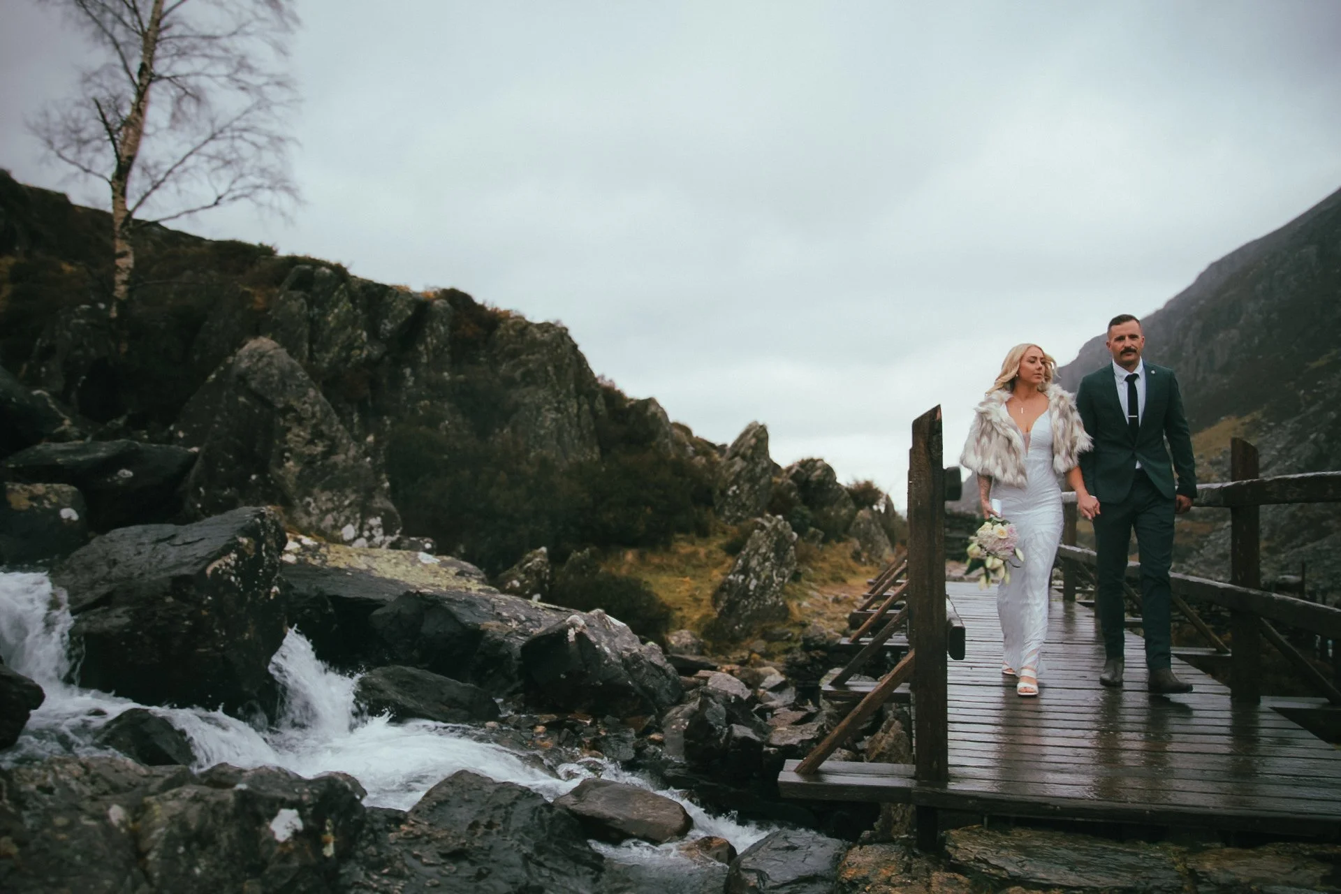 A couple on a wooden footbridge beside a rushing waterfall