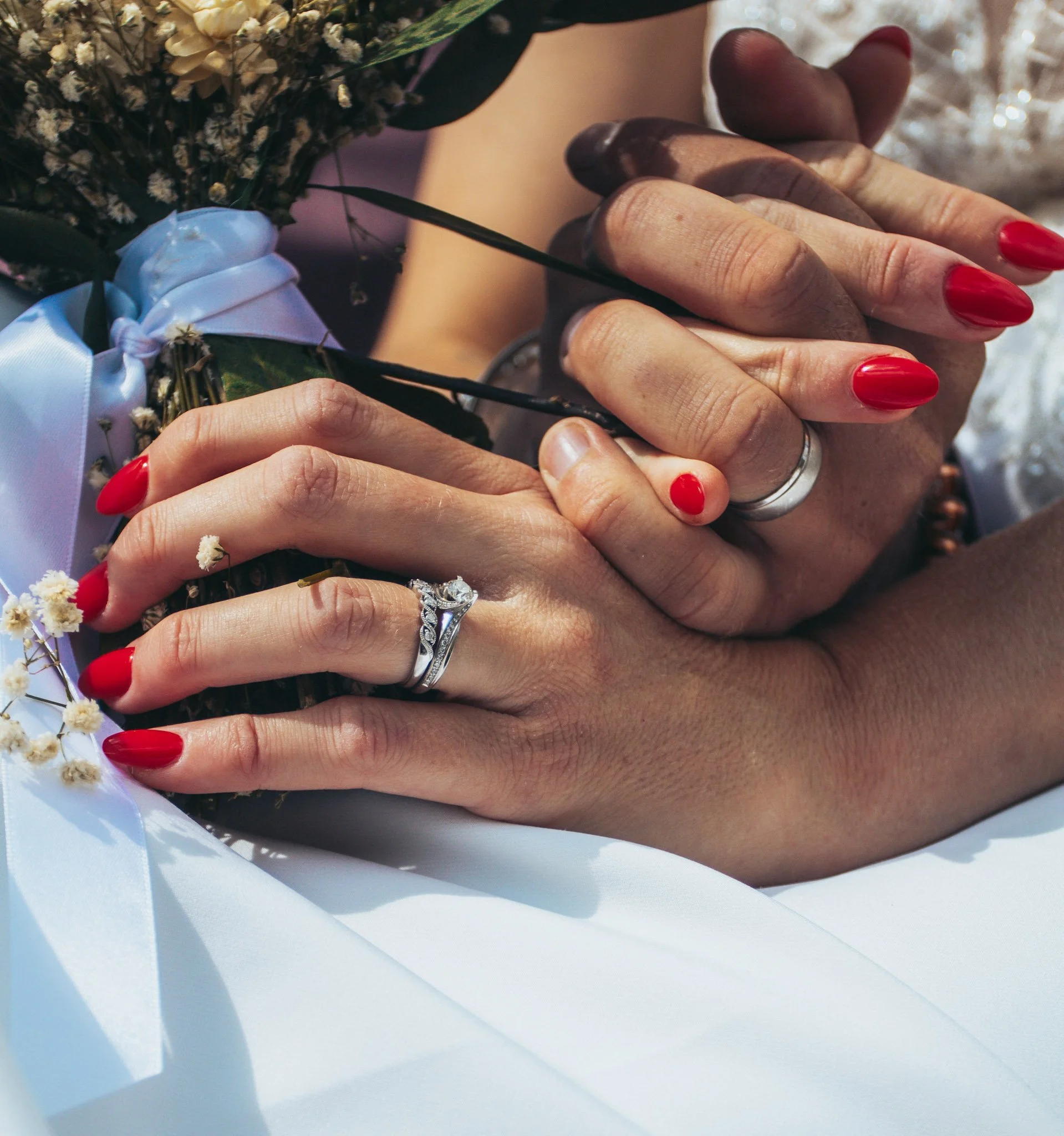 Close-up of a couple's hands showing a diamond engagement ring and red nail varnish
