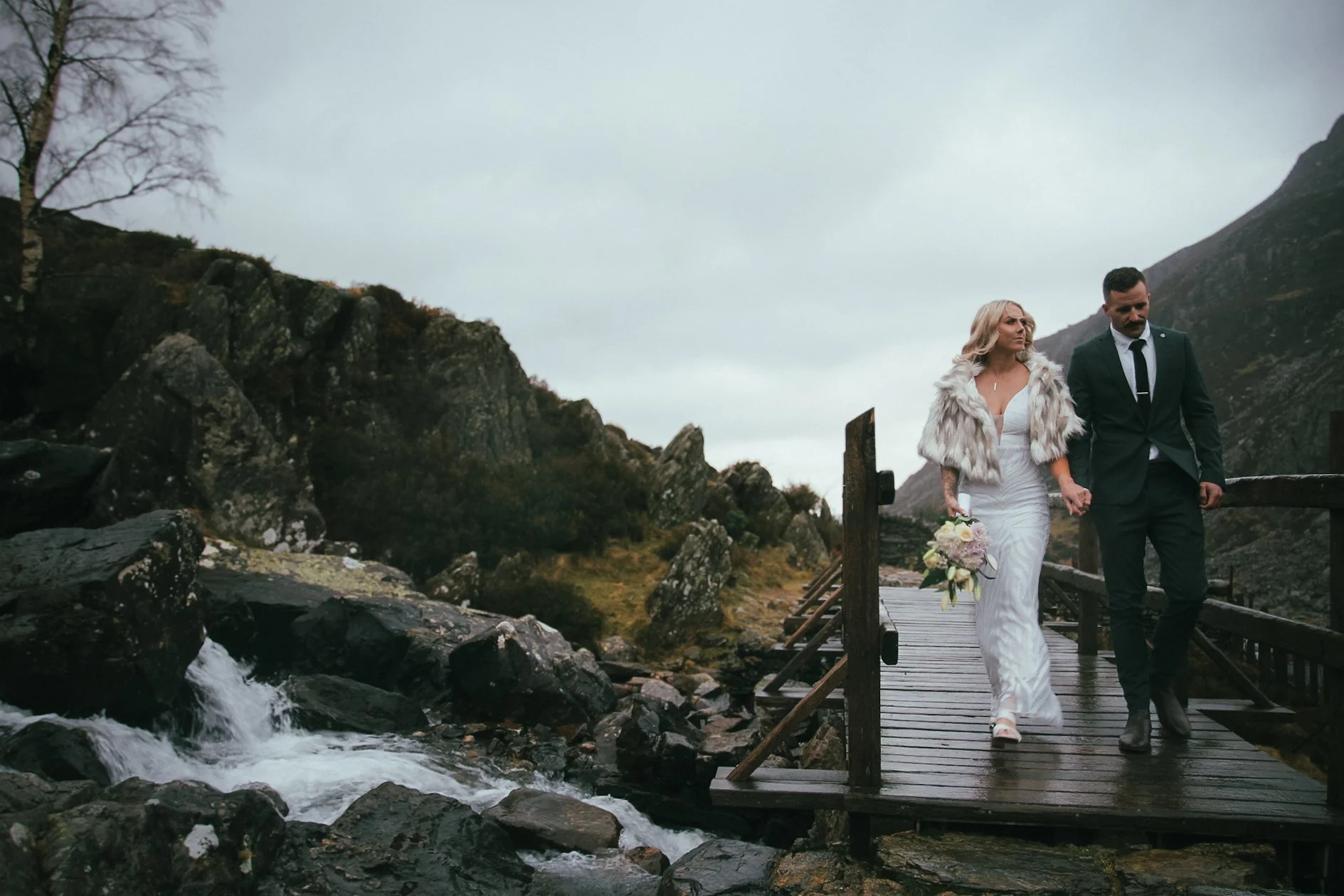 A couple walking across a wooden footbridge beside a waterfall