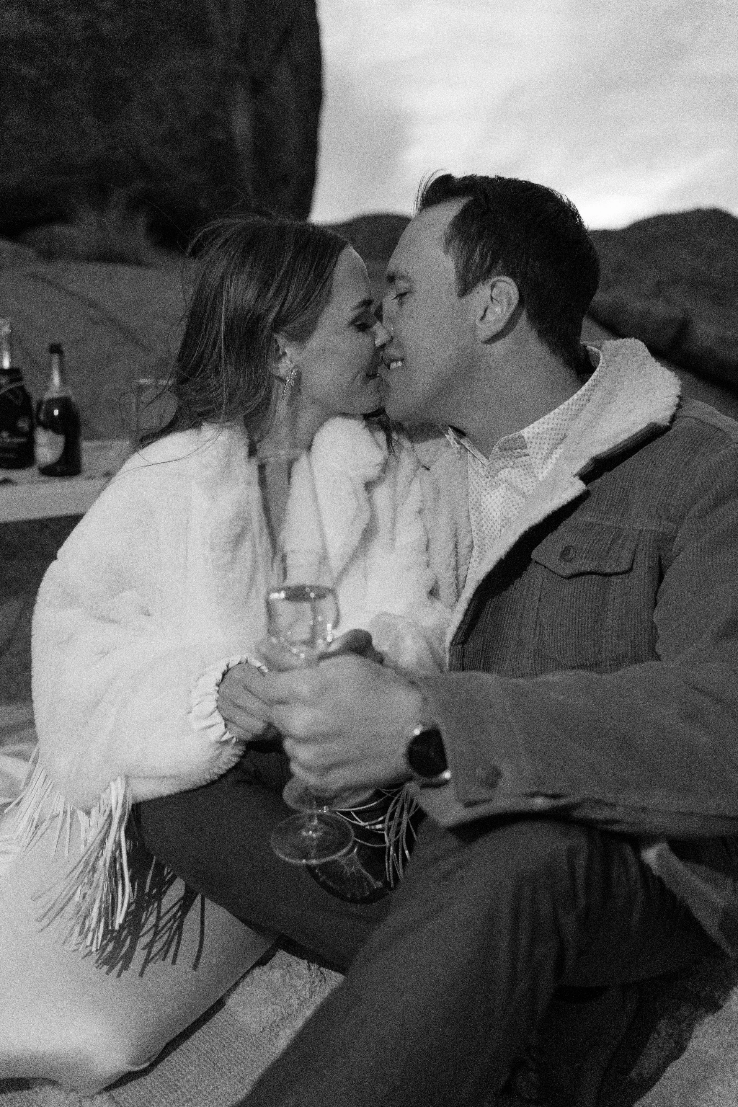 A couple kissing while holding glasses of champagne, in black and white
