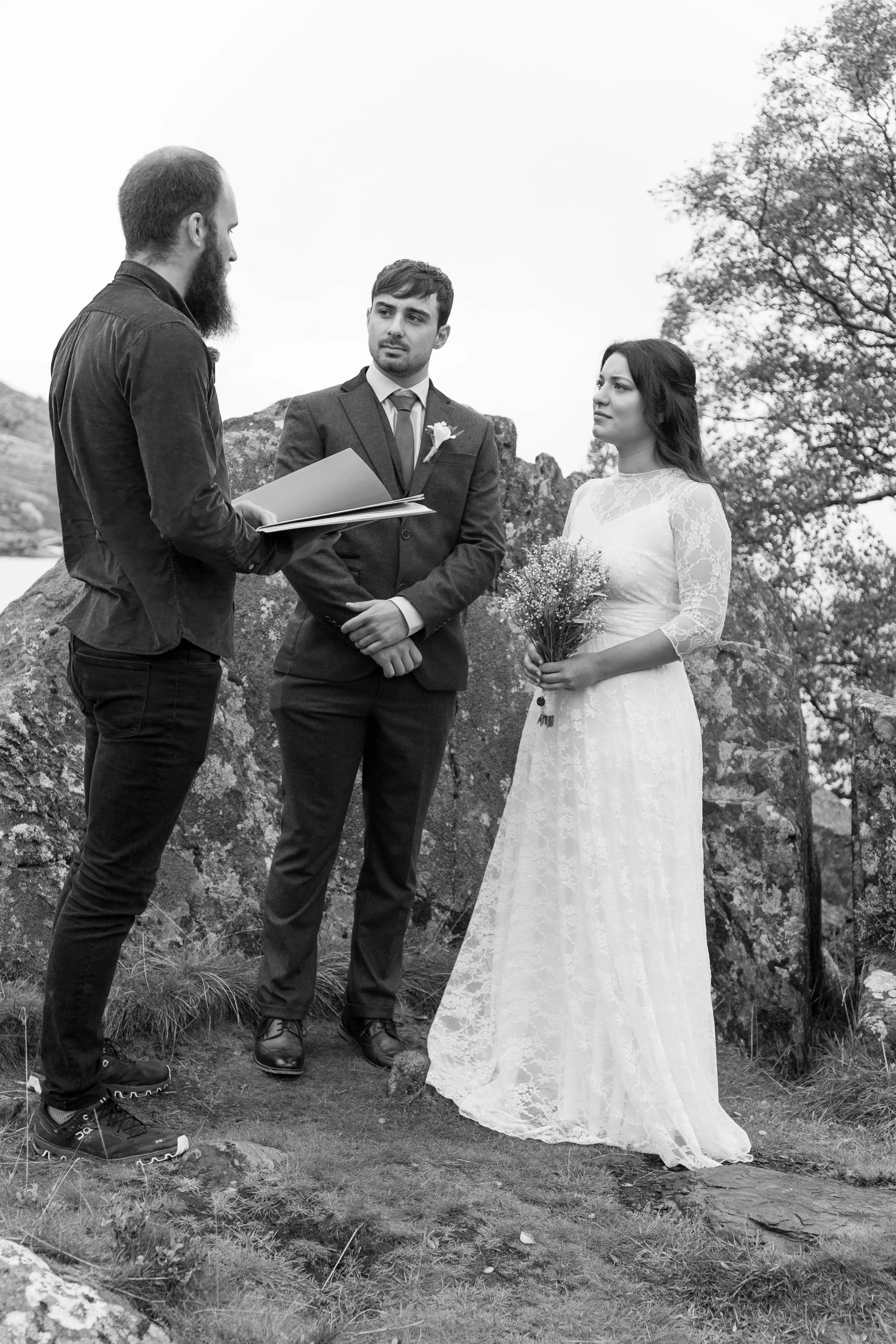 Black and white photo of Leon officiating a ceremony for a couple among trees