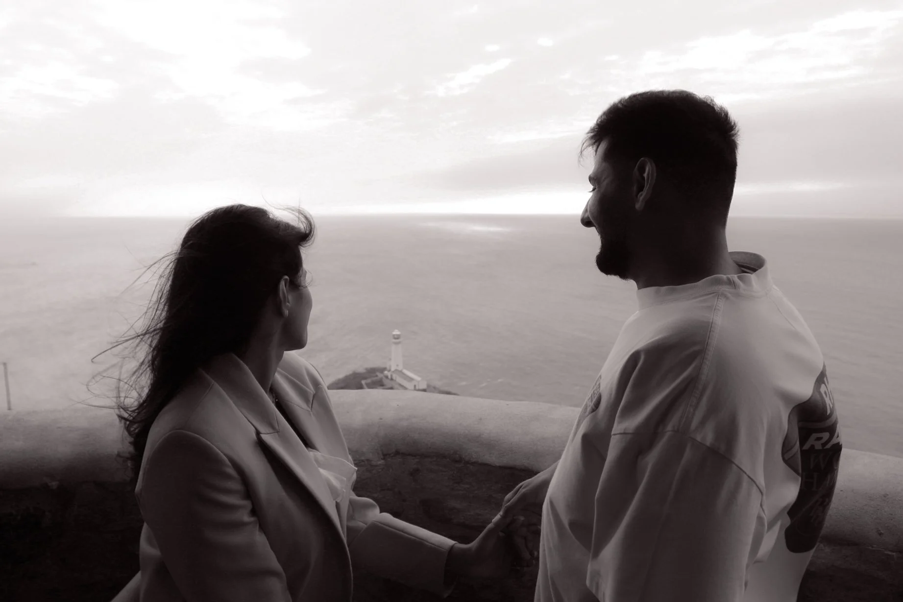 Couple sitting face to face on a clifftop overlooking the sea