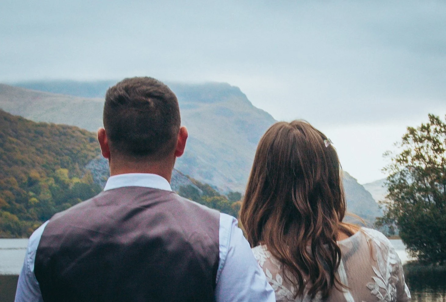 Couple seen from behind, looking out over wooded cliffs and the sea
