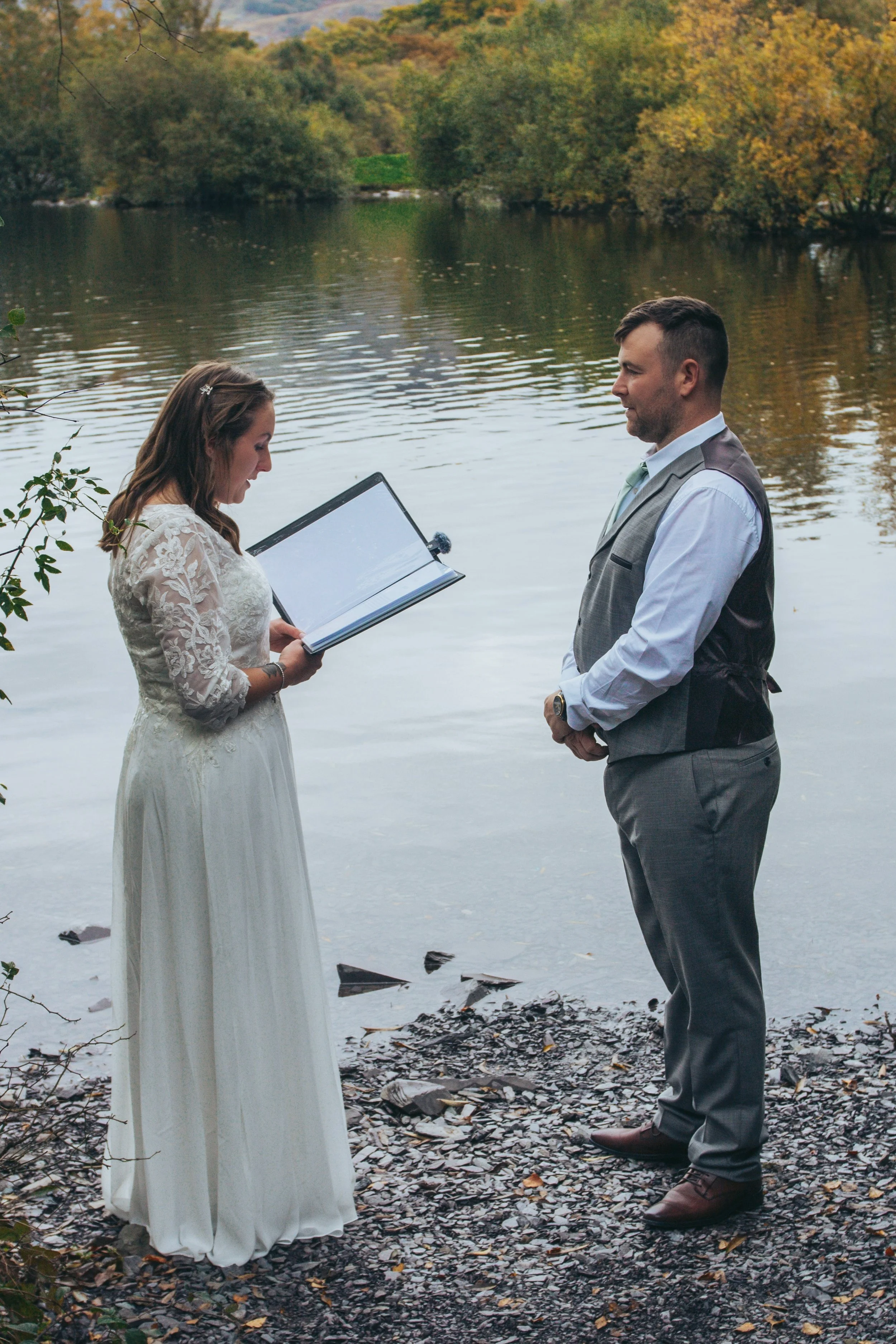 Couple reading vows to each other on a lakeshore