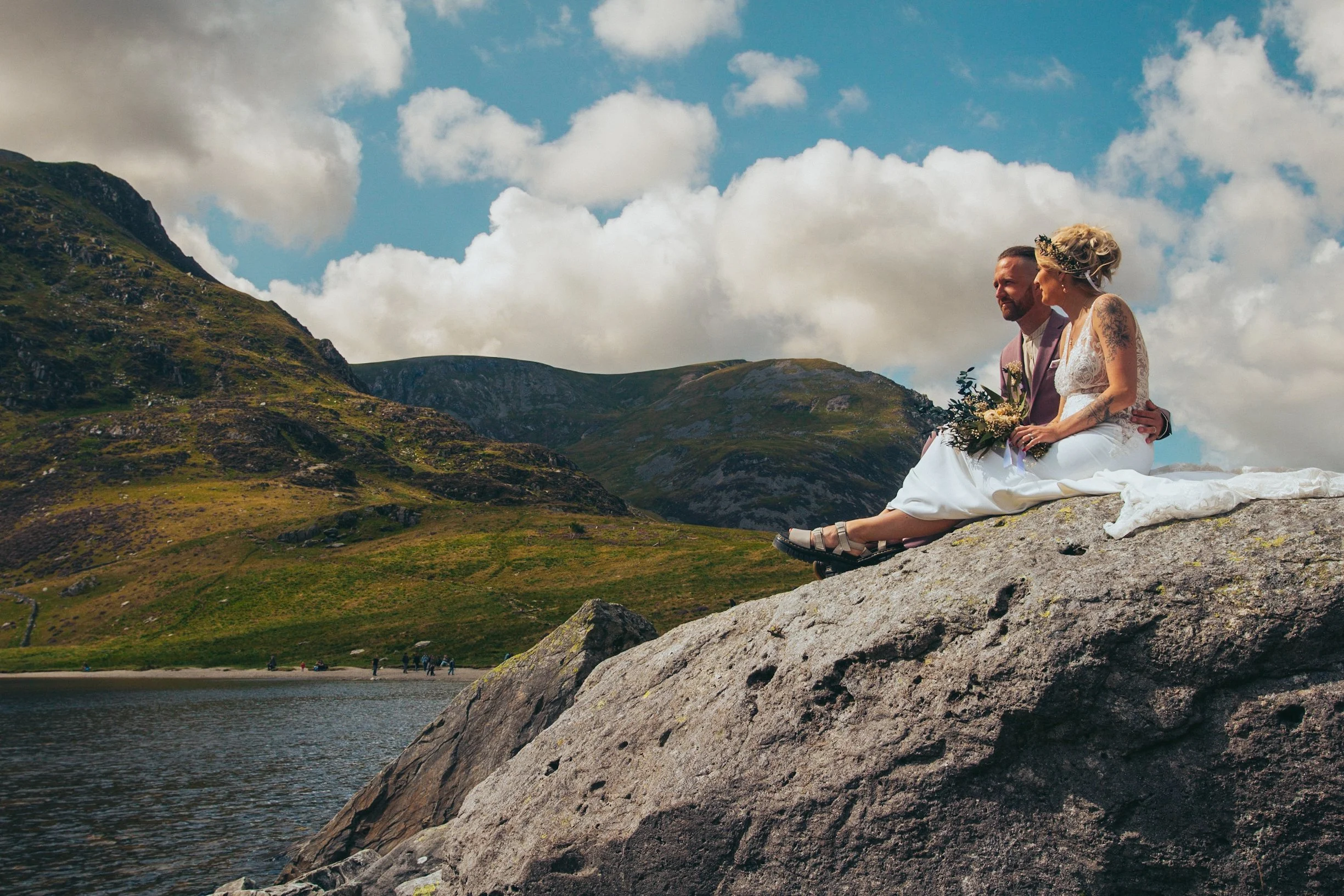 A couple sitting together on a rock above a lake with mountains behind