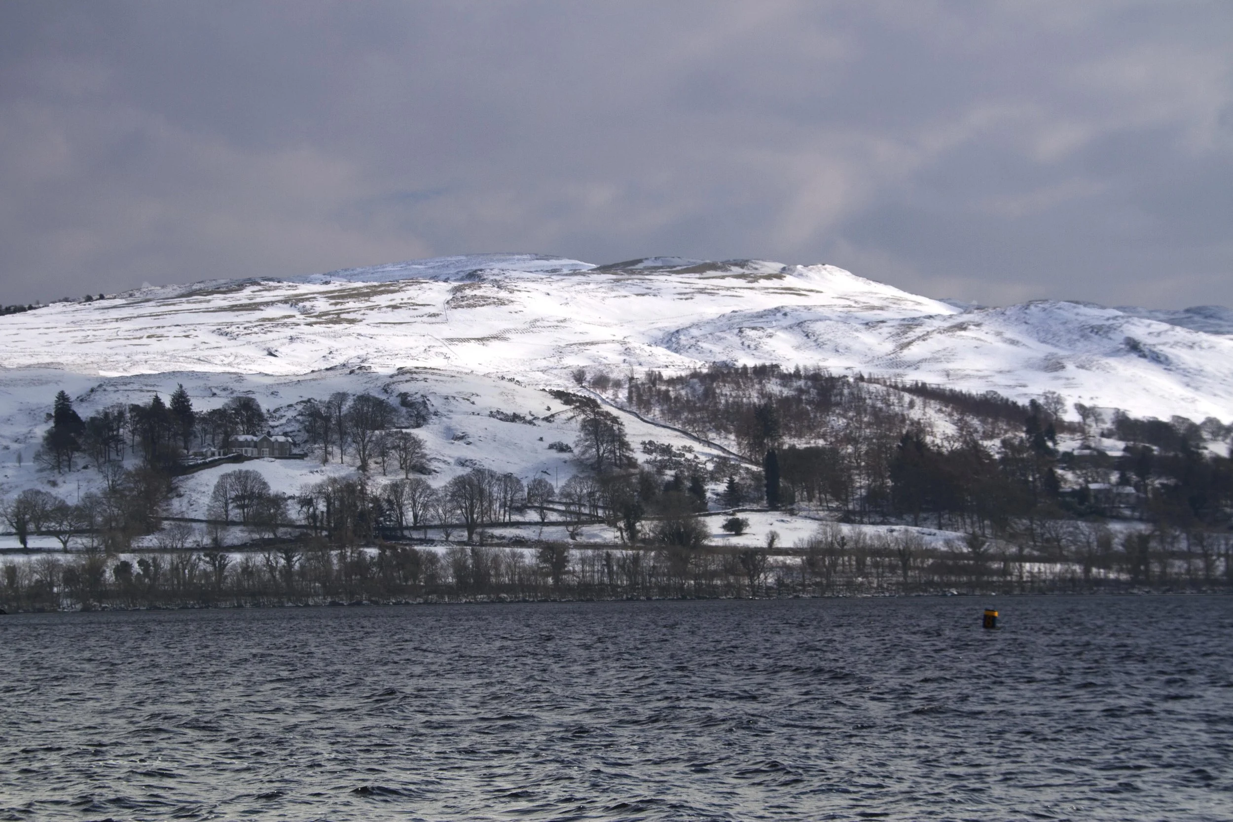 Snow-dusted hills rising above a dark lake under winter cloud