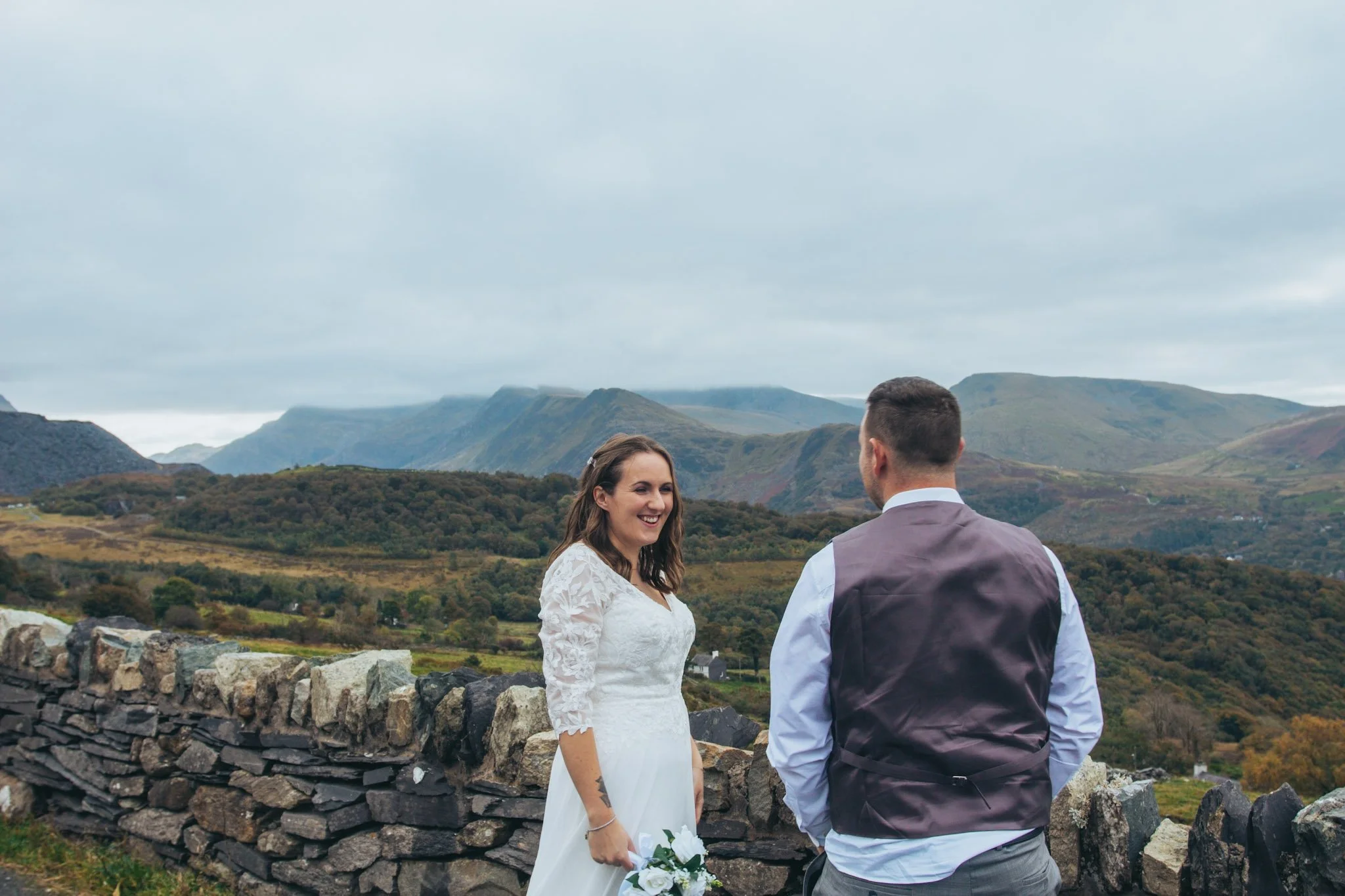 A couple standing by a dry stone wall with mountains behind them