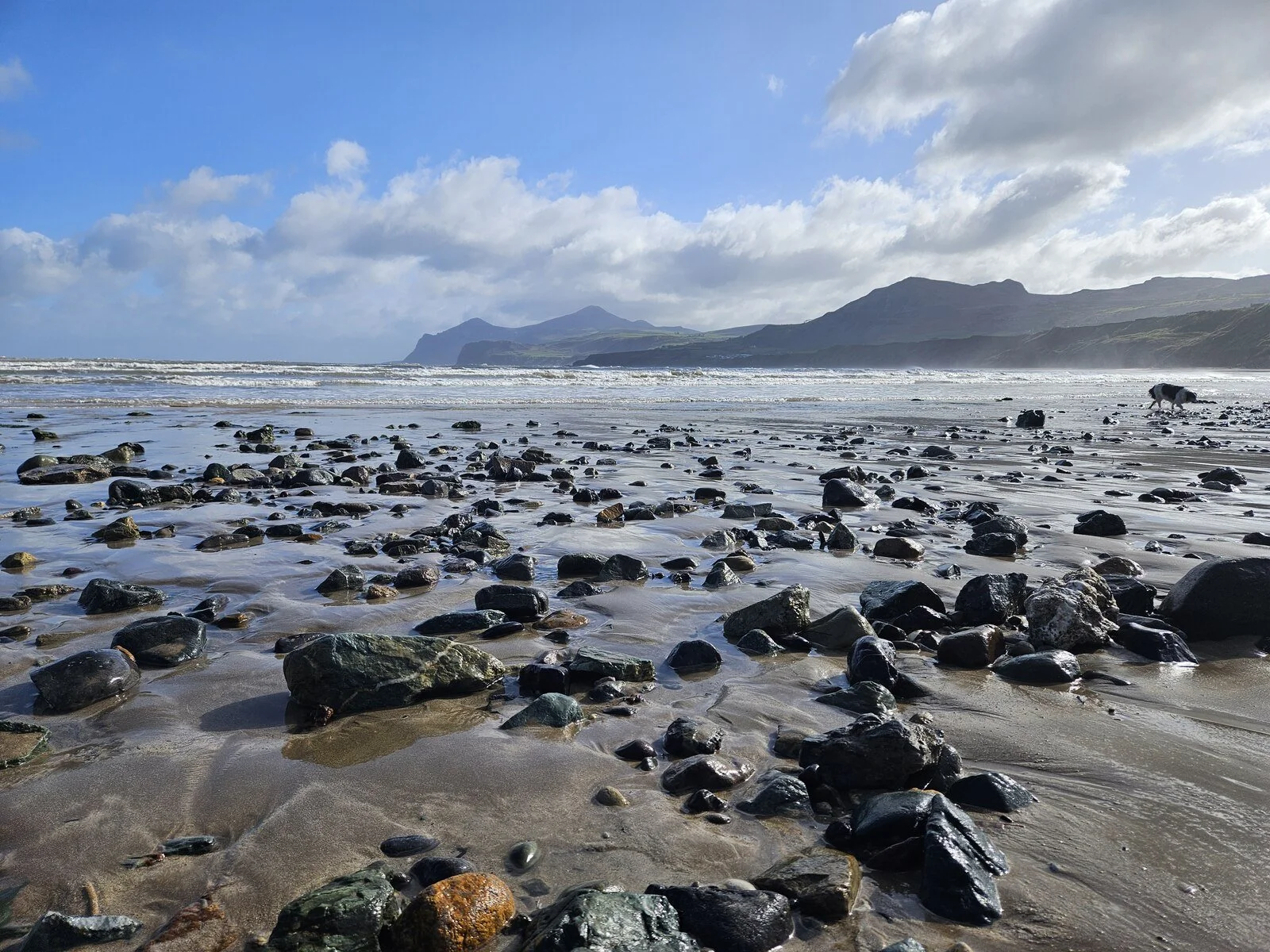 Walkers and open sand at Nefyn beach under a bright sky