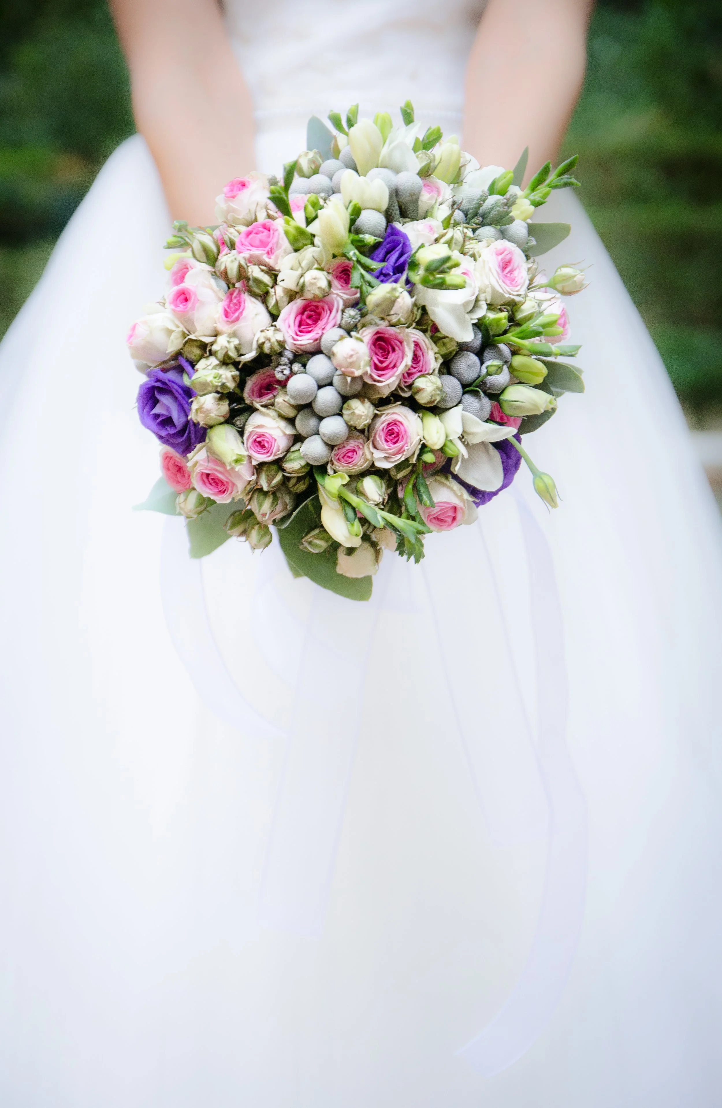 A bride holding a bouquet of pink, white and purple flowers against her white dress