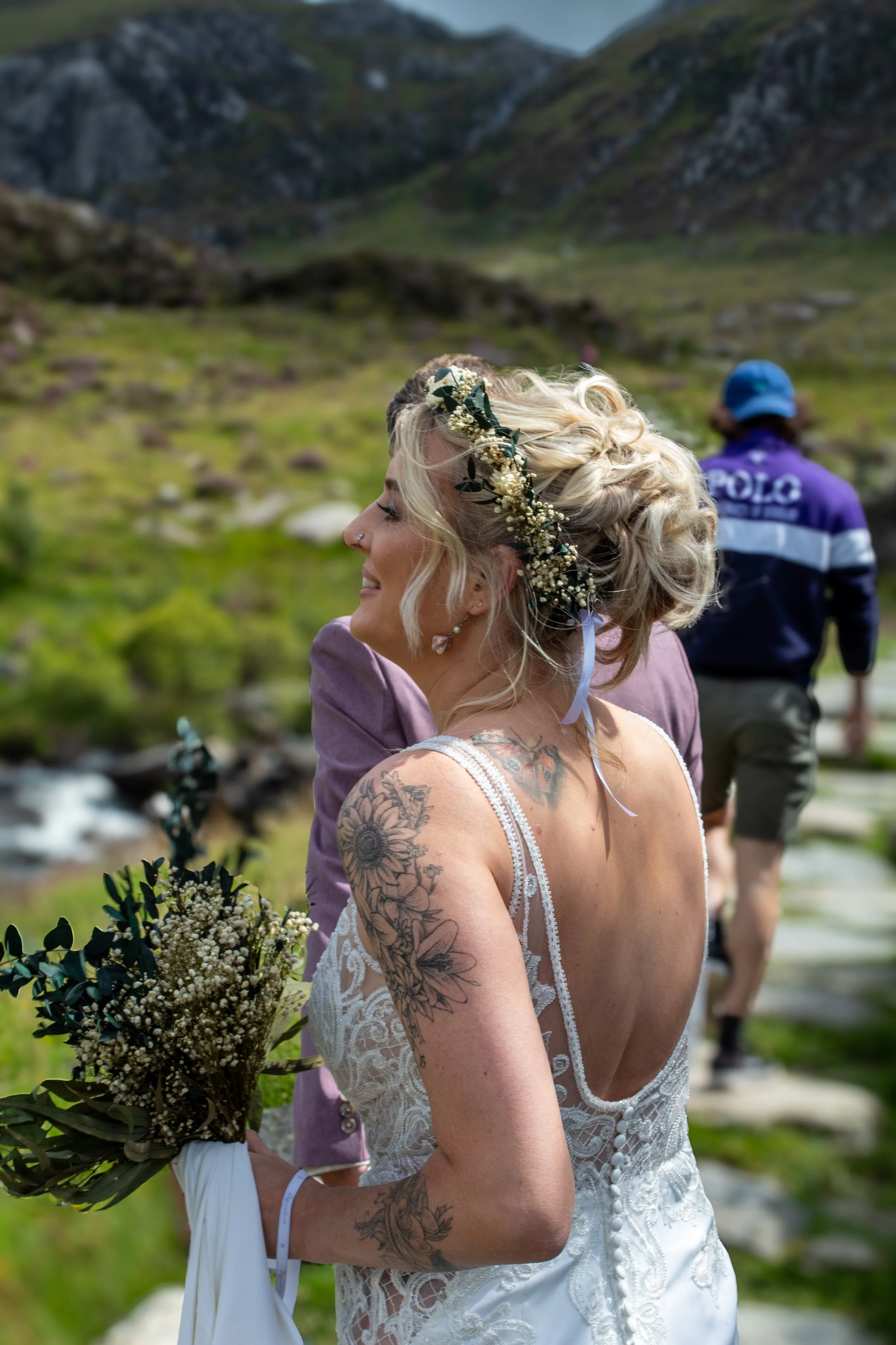 A bride with flowers in her hair, holding a bouquet, looking up on a mountain path