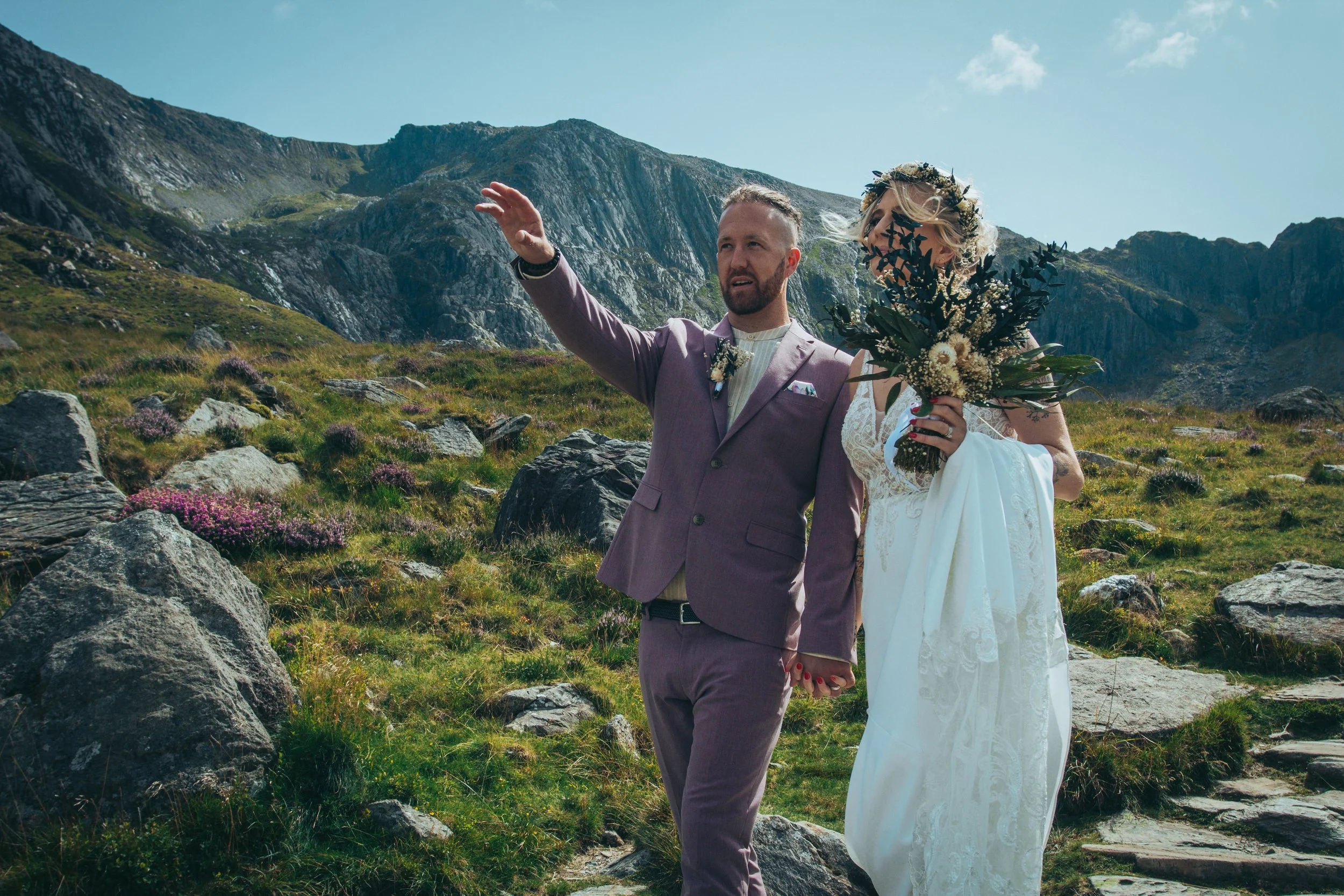 Couple on a rocky mountain path, the groom pointing out the view