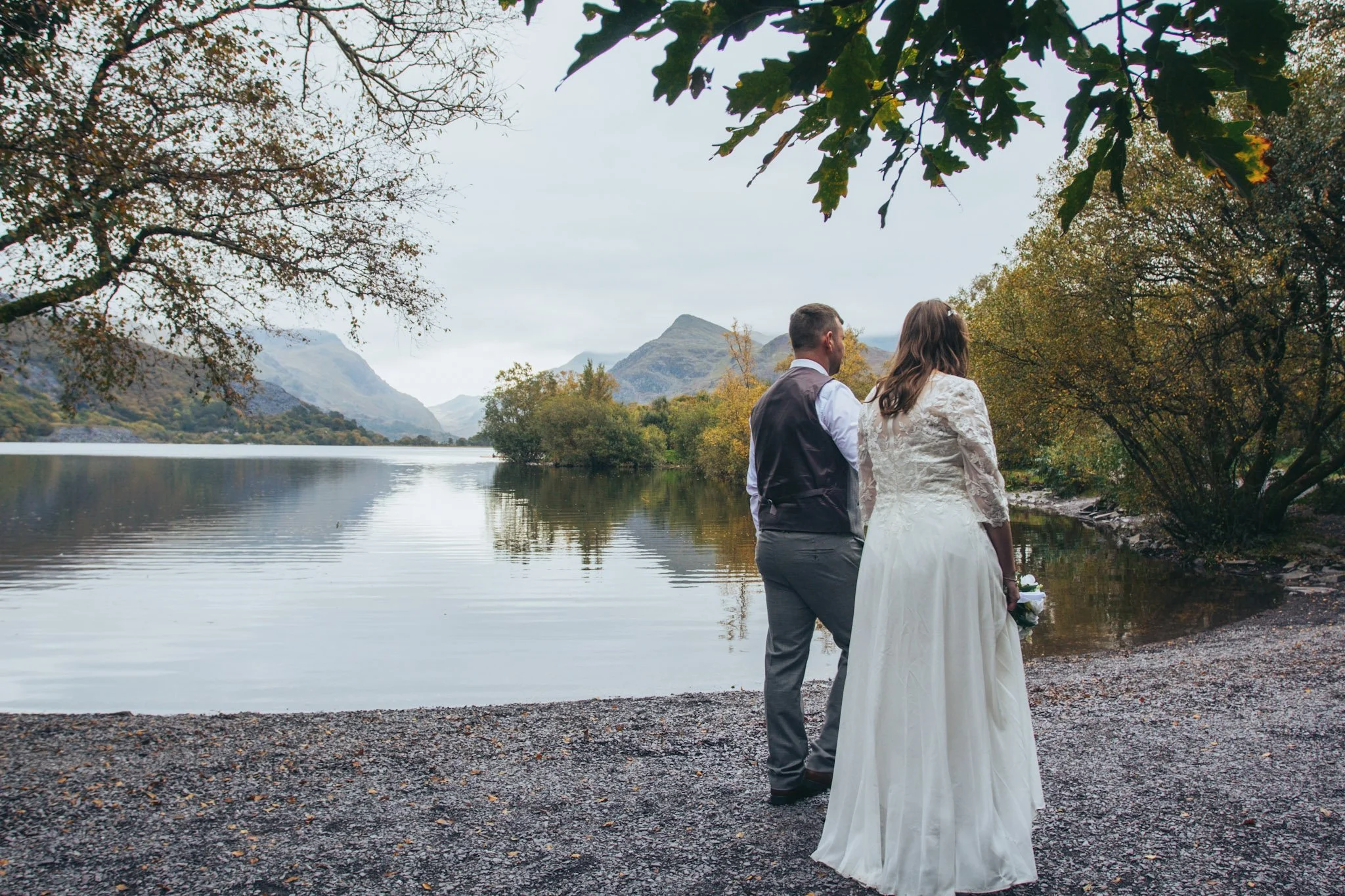 A couple walking together on a lakeshore beneath trees