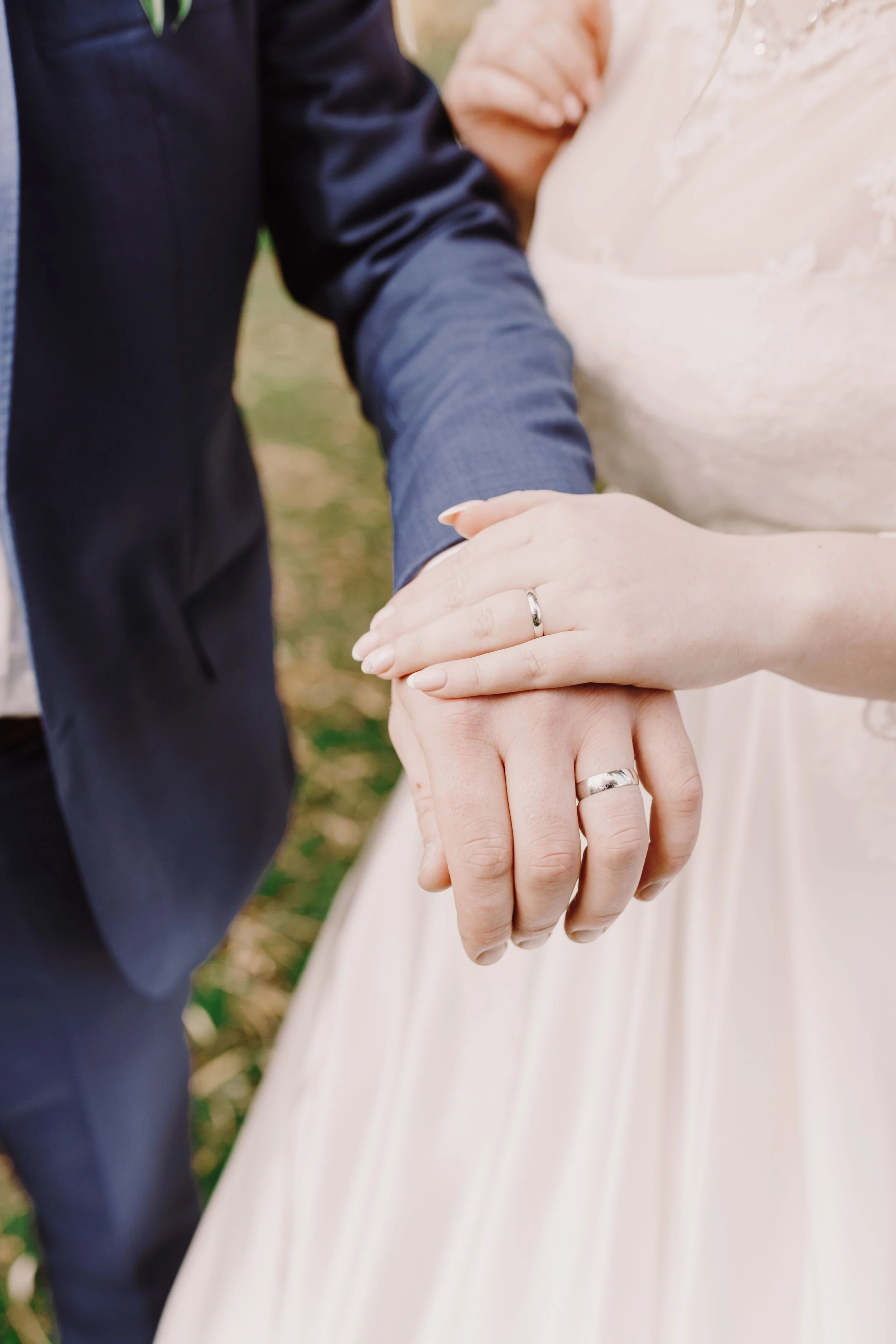 Close-up of a bride and groom holding hands, showing their wedding rings