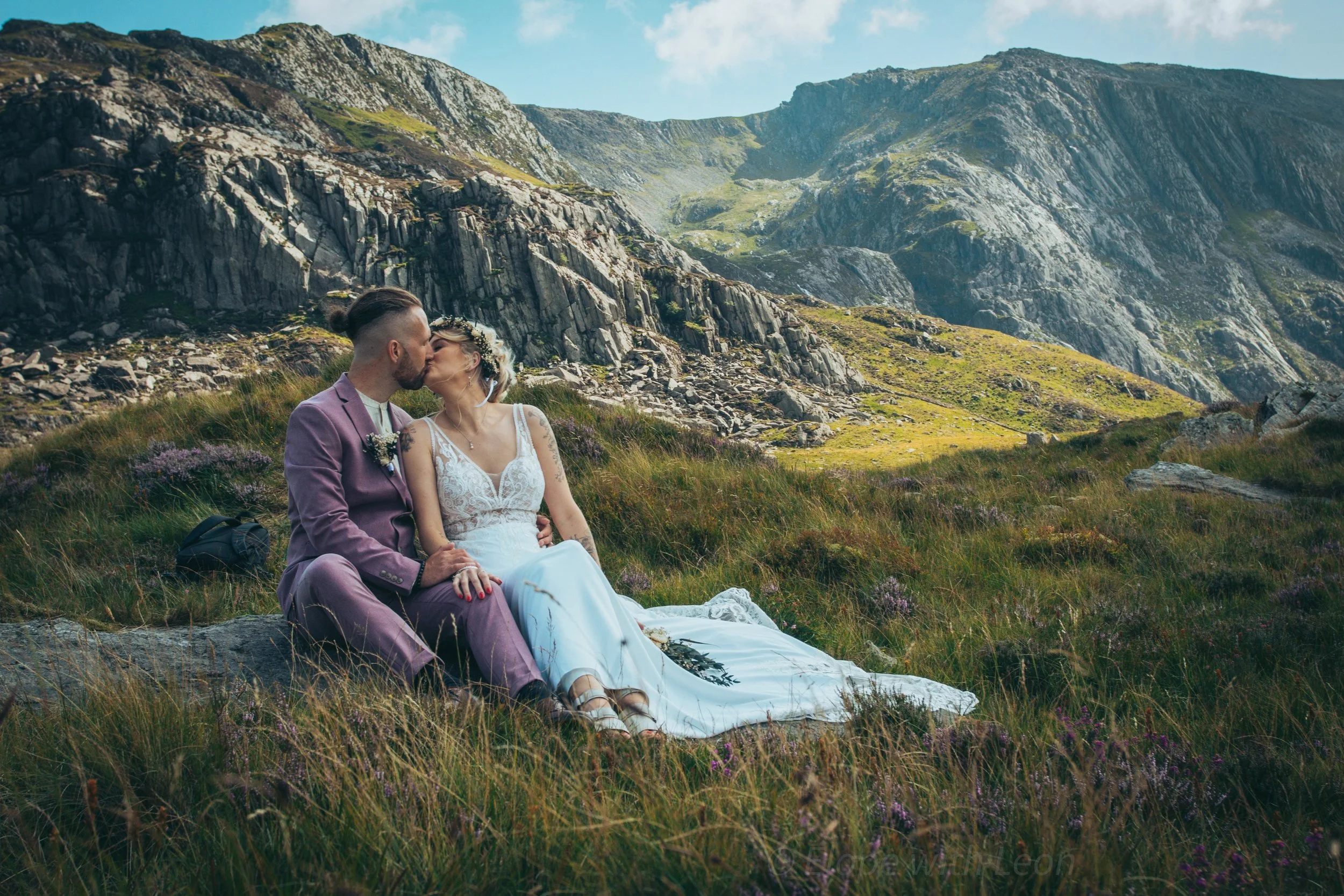 Dean and Tori kissing while sitting on the grass in a mountain valley
