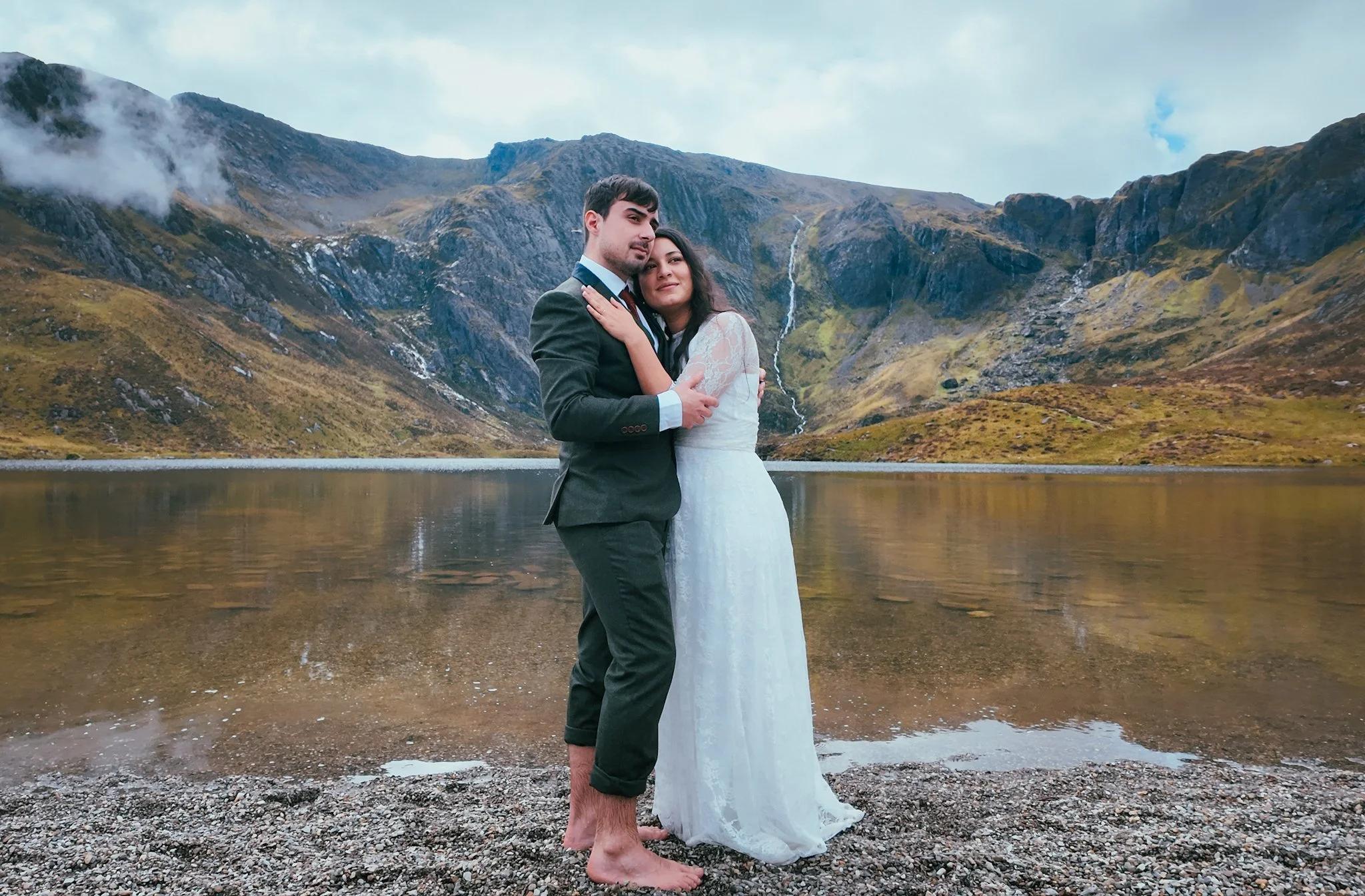 A couple embracing barefoot on the shore of a mountain lake