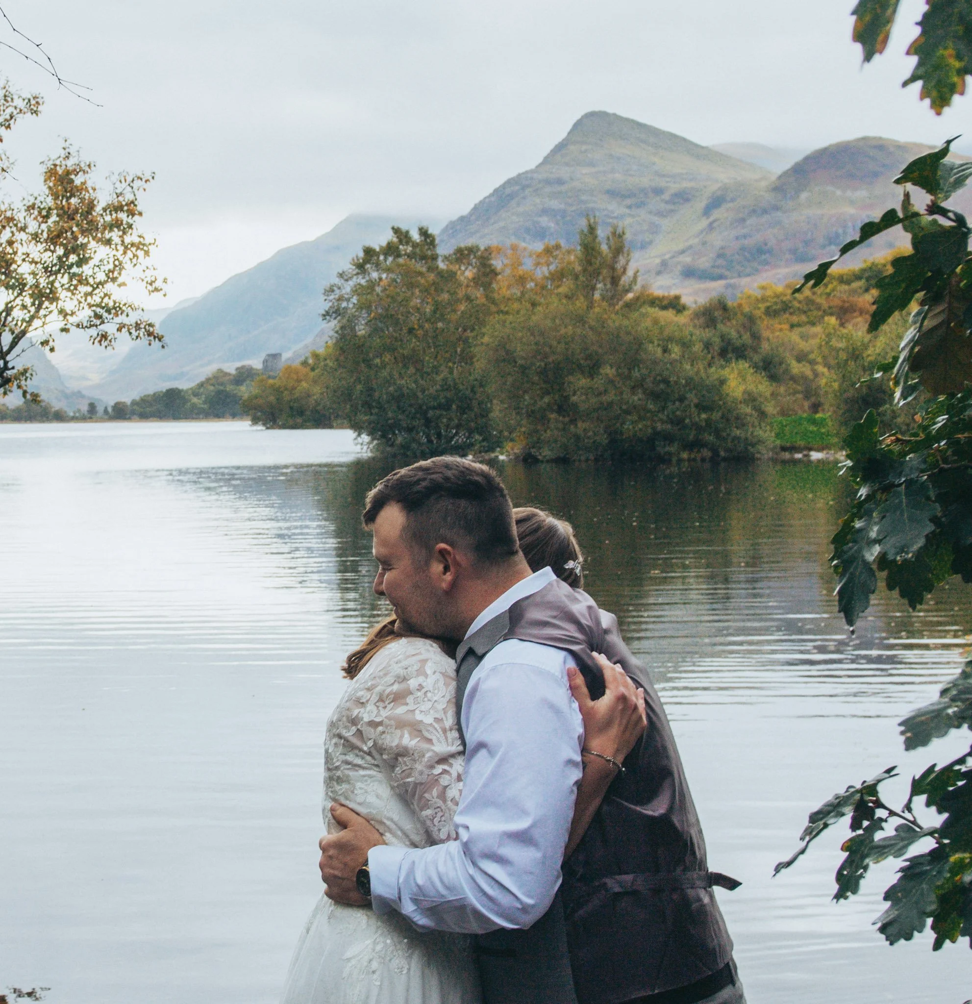 A couple embracing beside a lake with a mountain behind them
