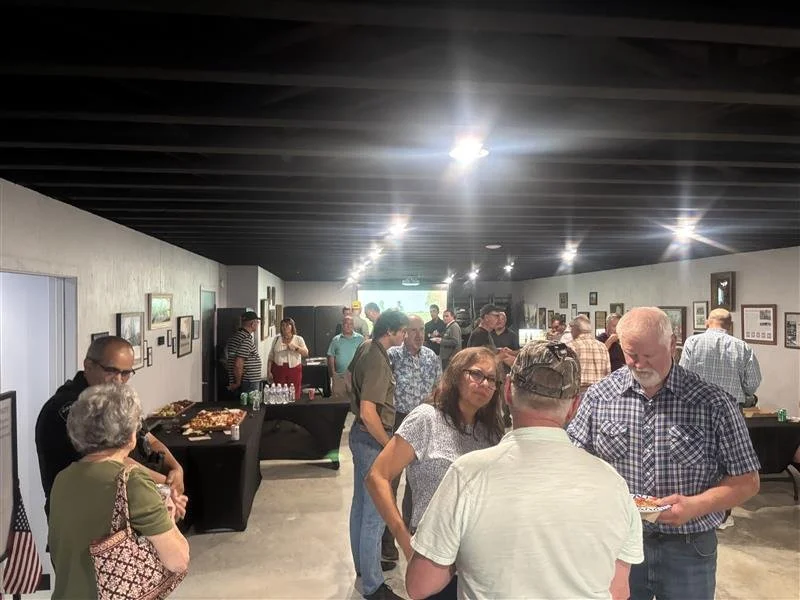 People socializing at a buffet-style gathering in an art gallery or event space with framed pictures on the walls.