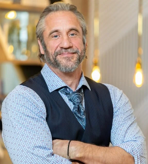 Gavin T. Elliot, Esq., founder and CEO of The Elliot Legal Group, PA, standing confidently in a law office wearing a blue checkered shirt, dark vest, and patterned tie, specializing in Florida estate planning and immigration law