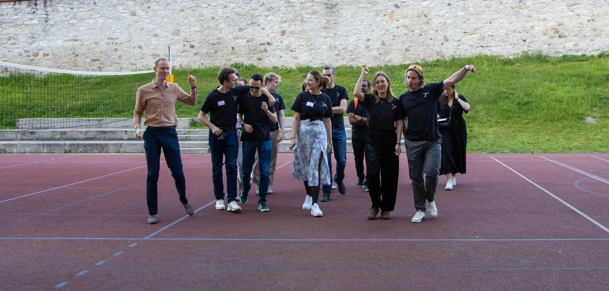 Group of people walking and talking on a sports court with a volleyball net and grassy hill in the background.
