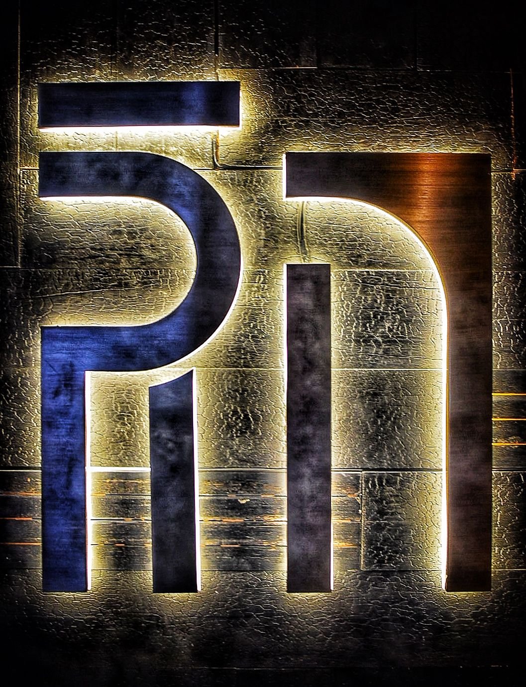 Illuminated decorative sign with the letters 'PI' backlit against a textured wall.