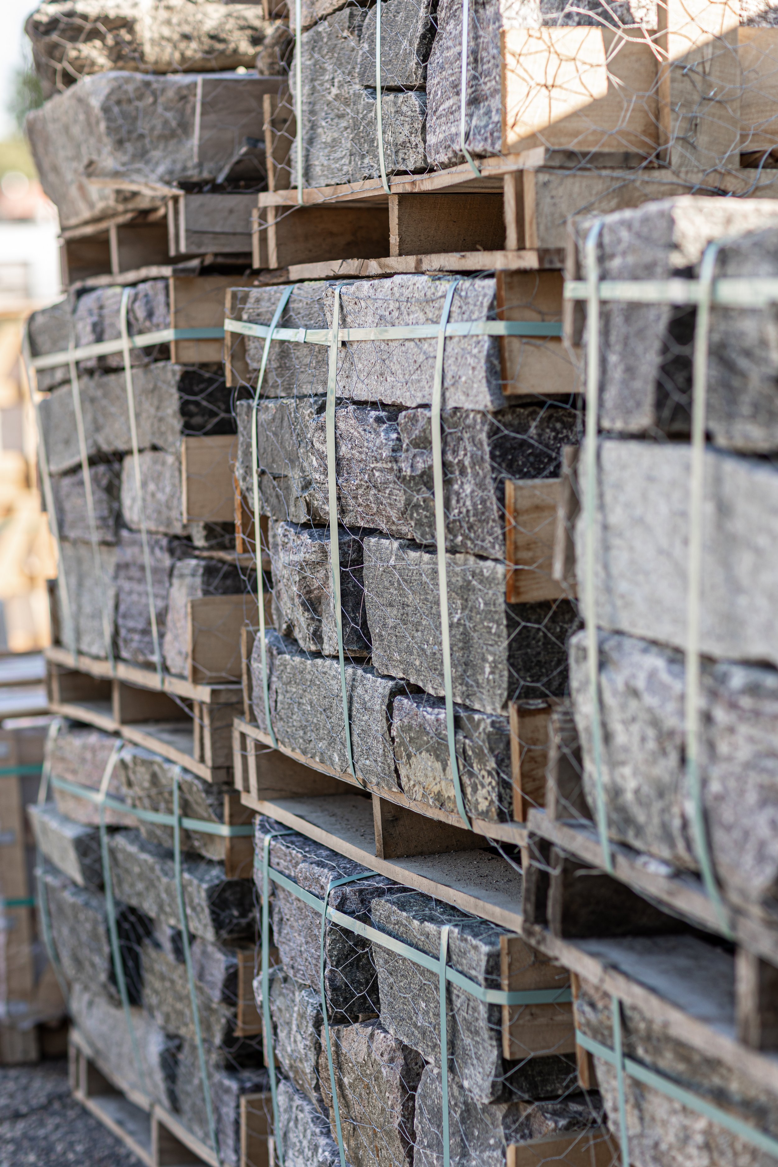 A stack of large, cut stone slabs on wooden pallets, secured with metal wire, outdoors.