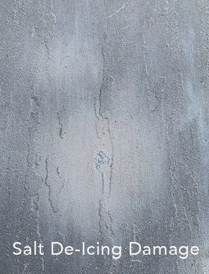 Close-up of a concrete surface with salt de-icing damage, showing cracks and rough patches.