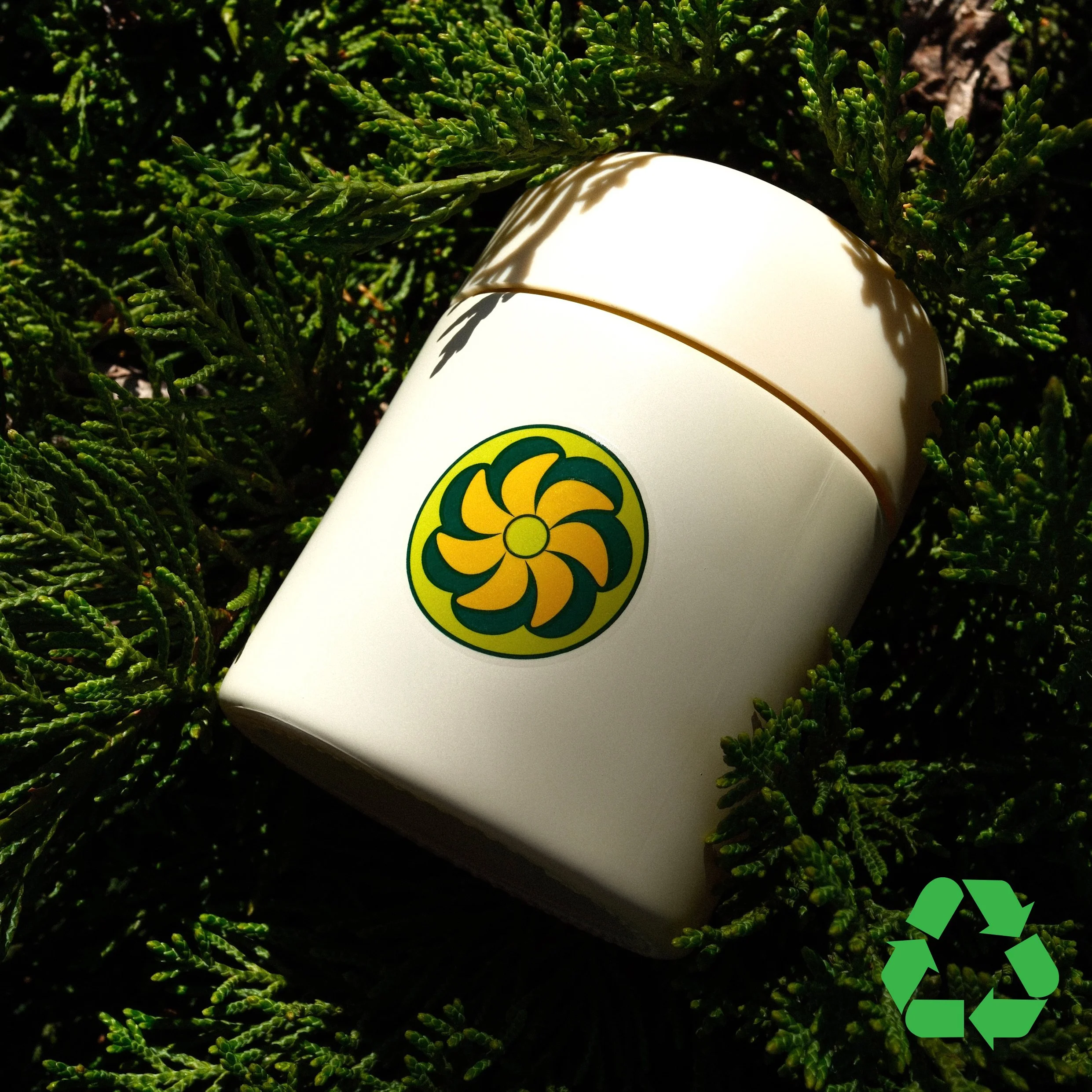 A white container with a yellow and green emblem is lying on dark soil, surrounded by lush green foliage.