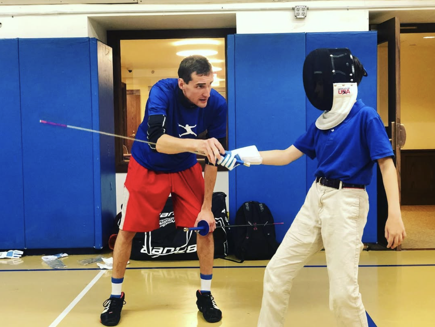Several fencers practicing sword fencing on a gym indoor foil fencing piste.