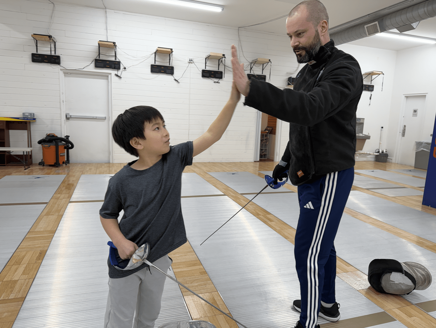 Young TMFC fencer high-fiving a coach after a lesson