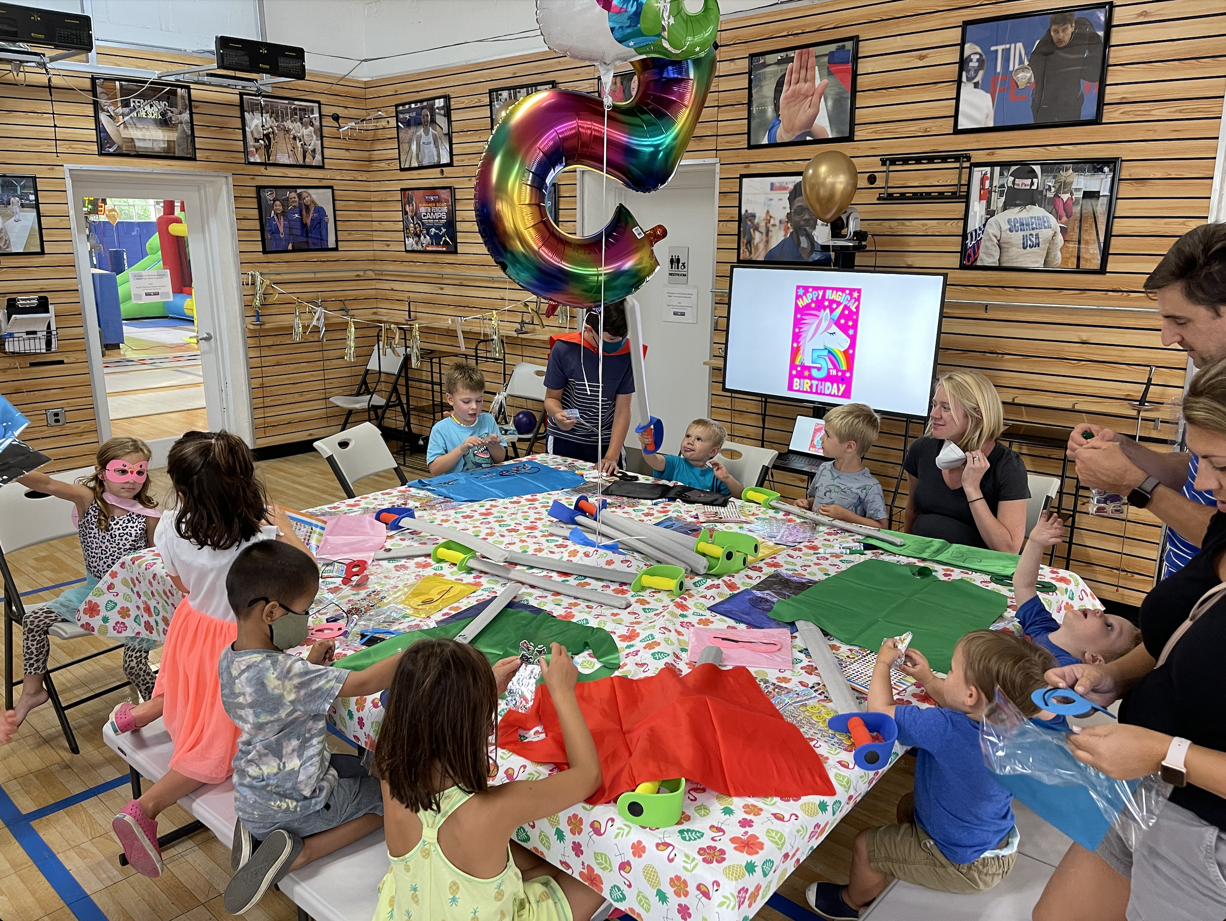 A fencing birthday party at TMFC with kids gathered around a craft table and a unicorn balloon