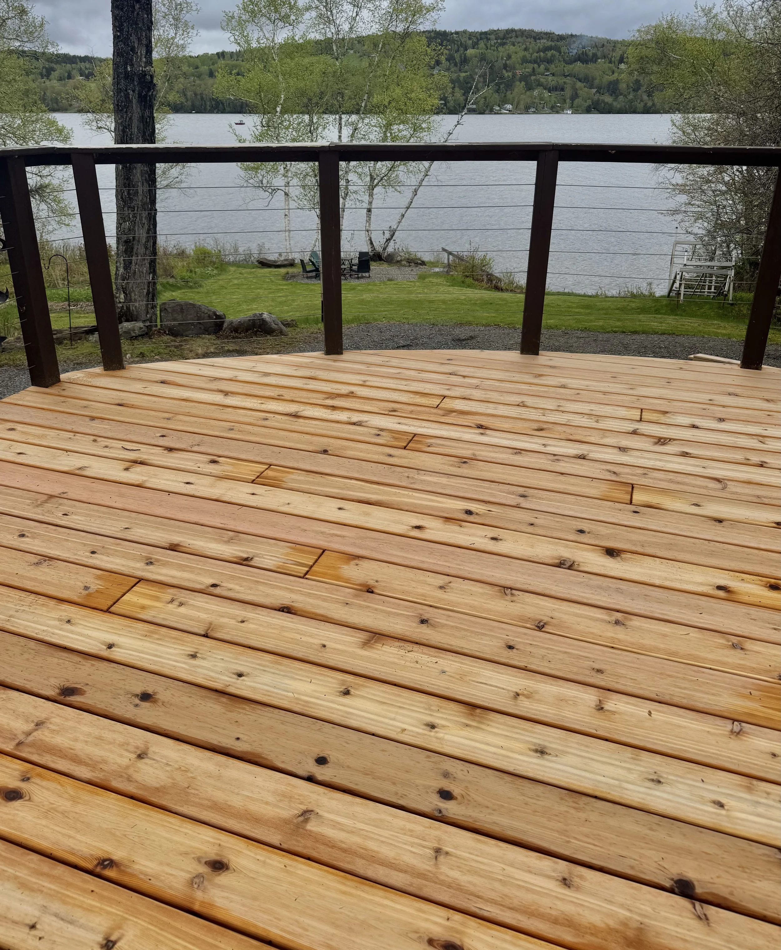 Wooden deck overlooking a grassy yard and a large body of water with trees and hills in the background.